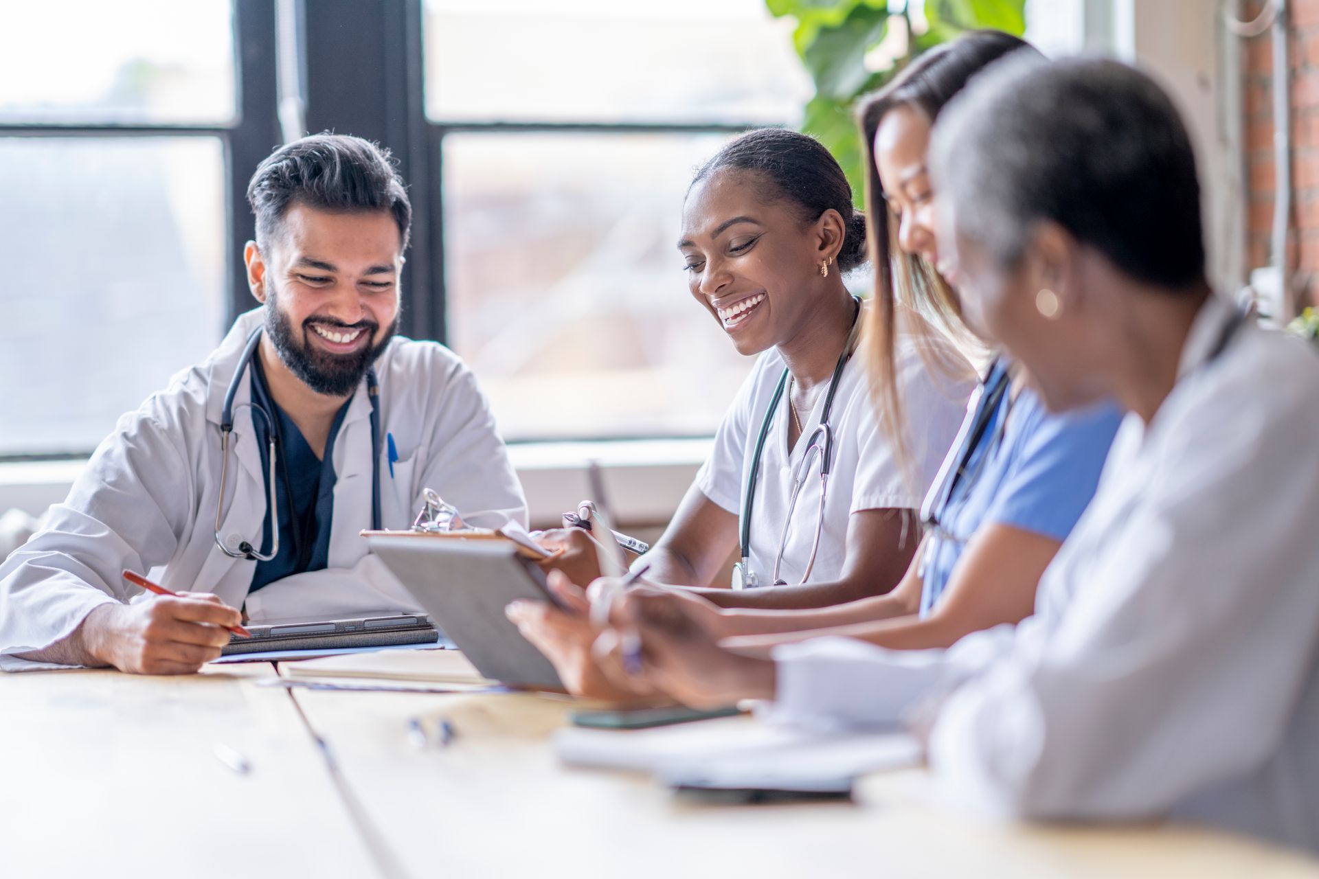 A group of doctors and nurses are sitting around a table looking at a tablet.