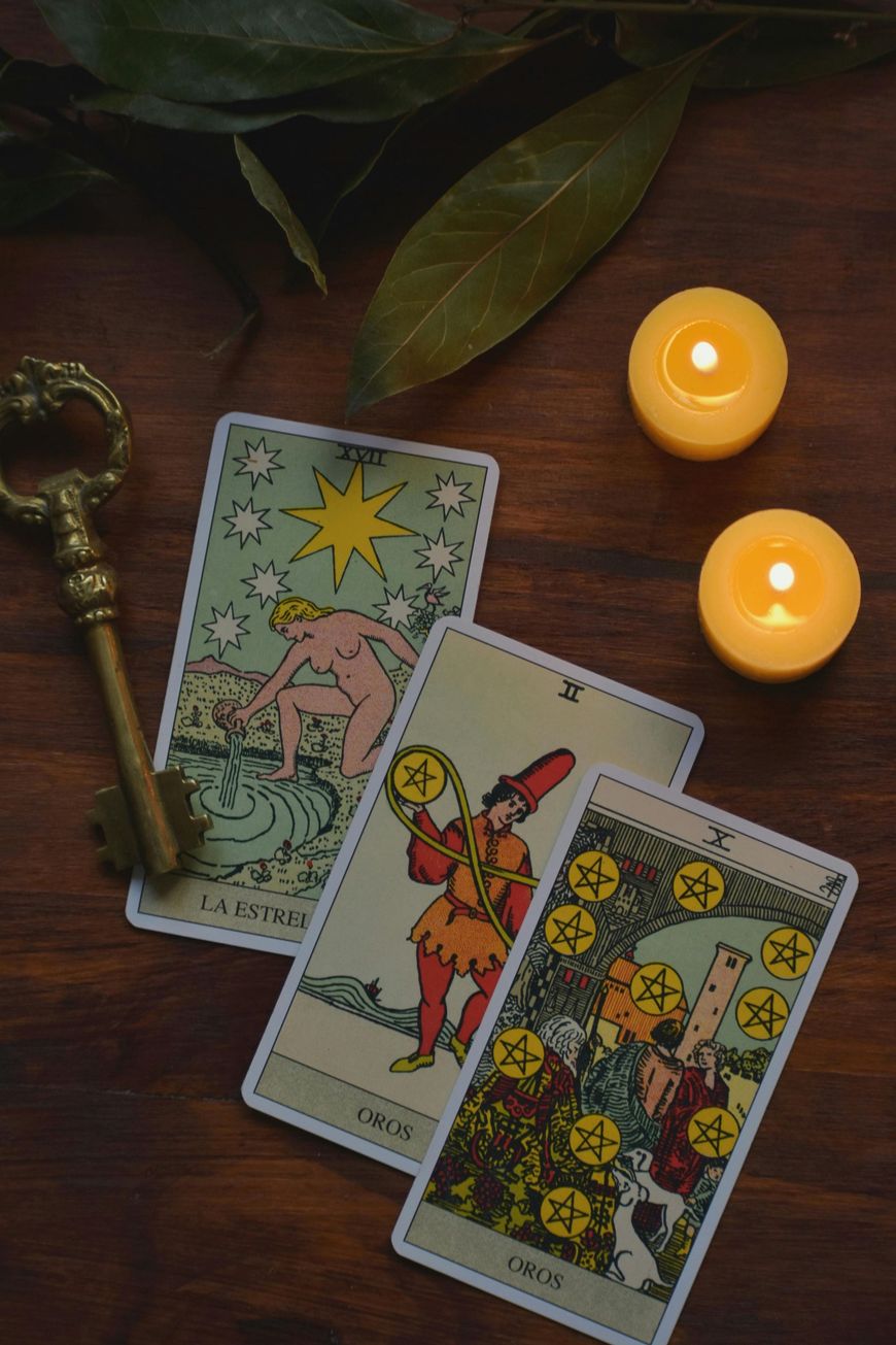Trois cartes de tarot sur une table en bois, à côté de deux bougies allumées et d'une clé en laiton.