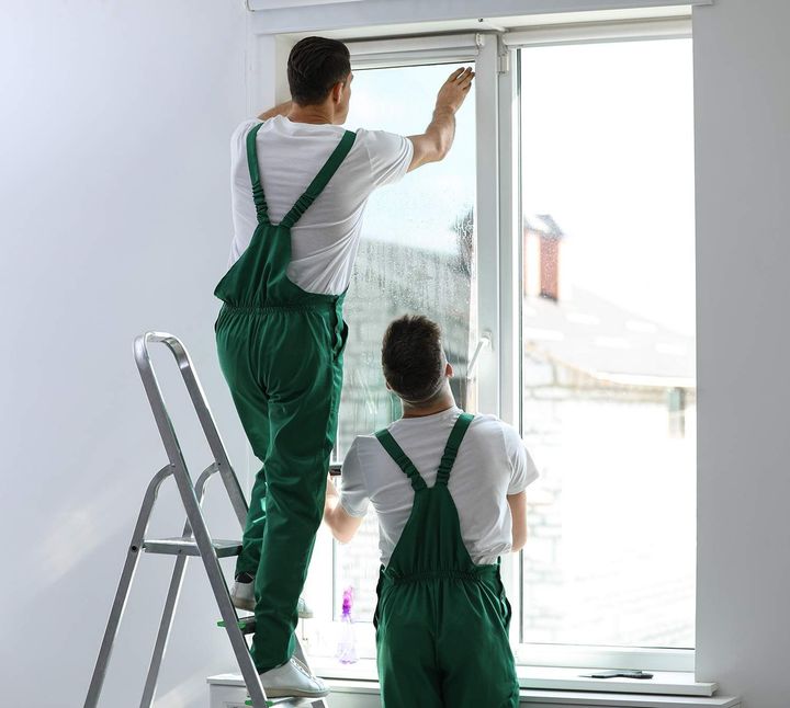 two men are standing on a ladder cleaning a window .