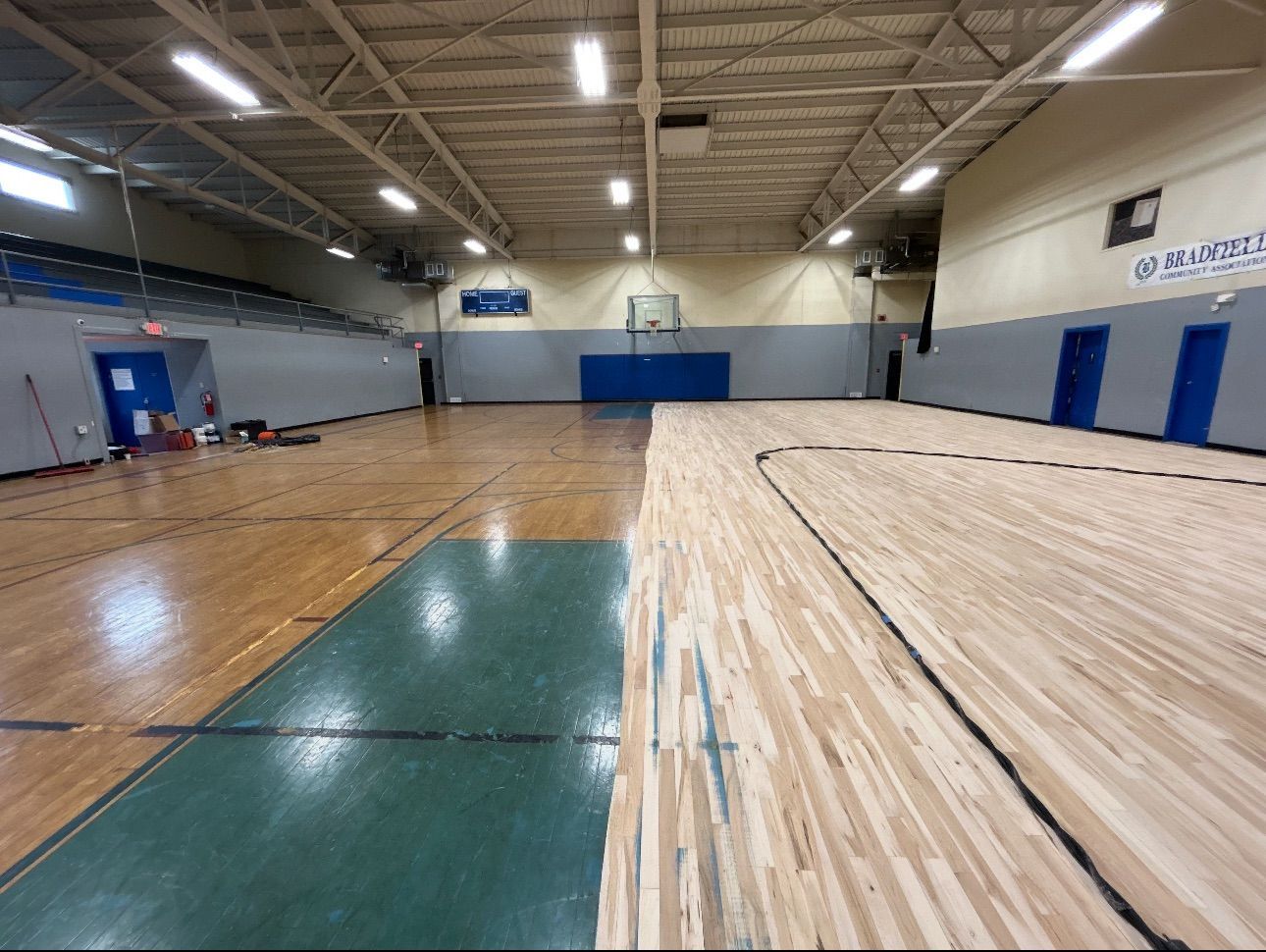 Basketball court with wood floor, partially refinished. Green and blue painted areas.