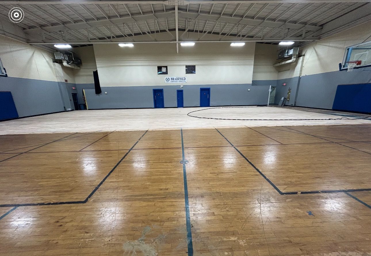 Wooden basketball court in a gymnasium, with blue wall padding and doors.