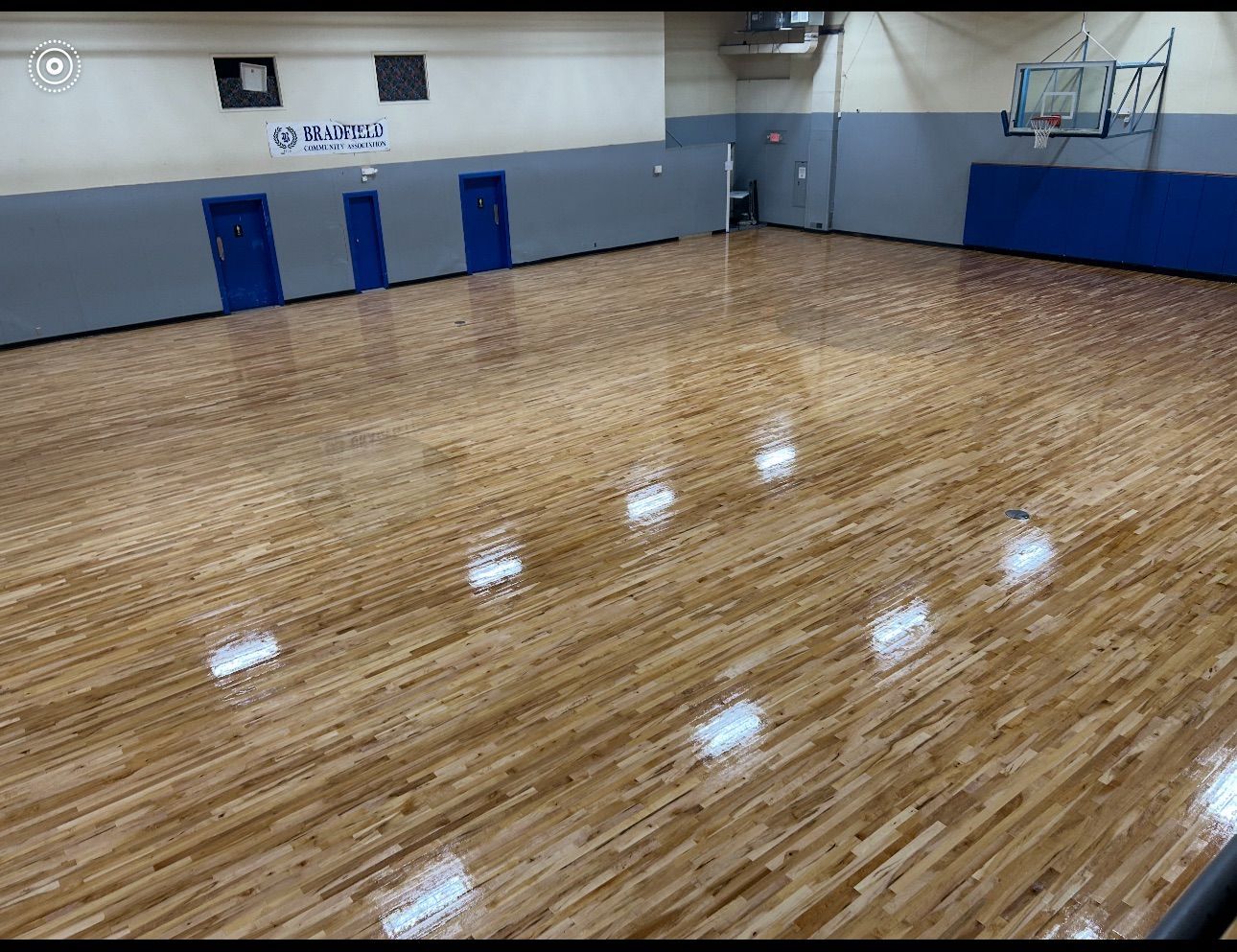 Empty gymnasium with polished wooden floor, blue and gray walls, and basketball hoop.