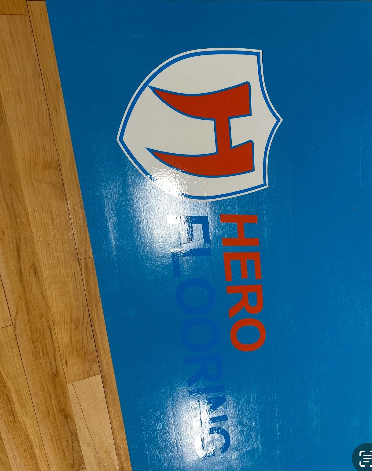 Hero Flooring logo on blue surface: shield with a stylized 