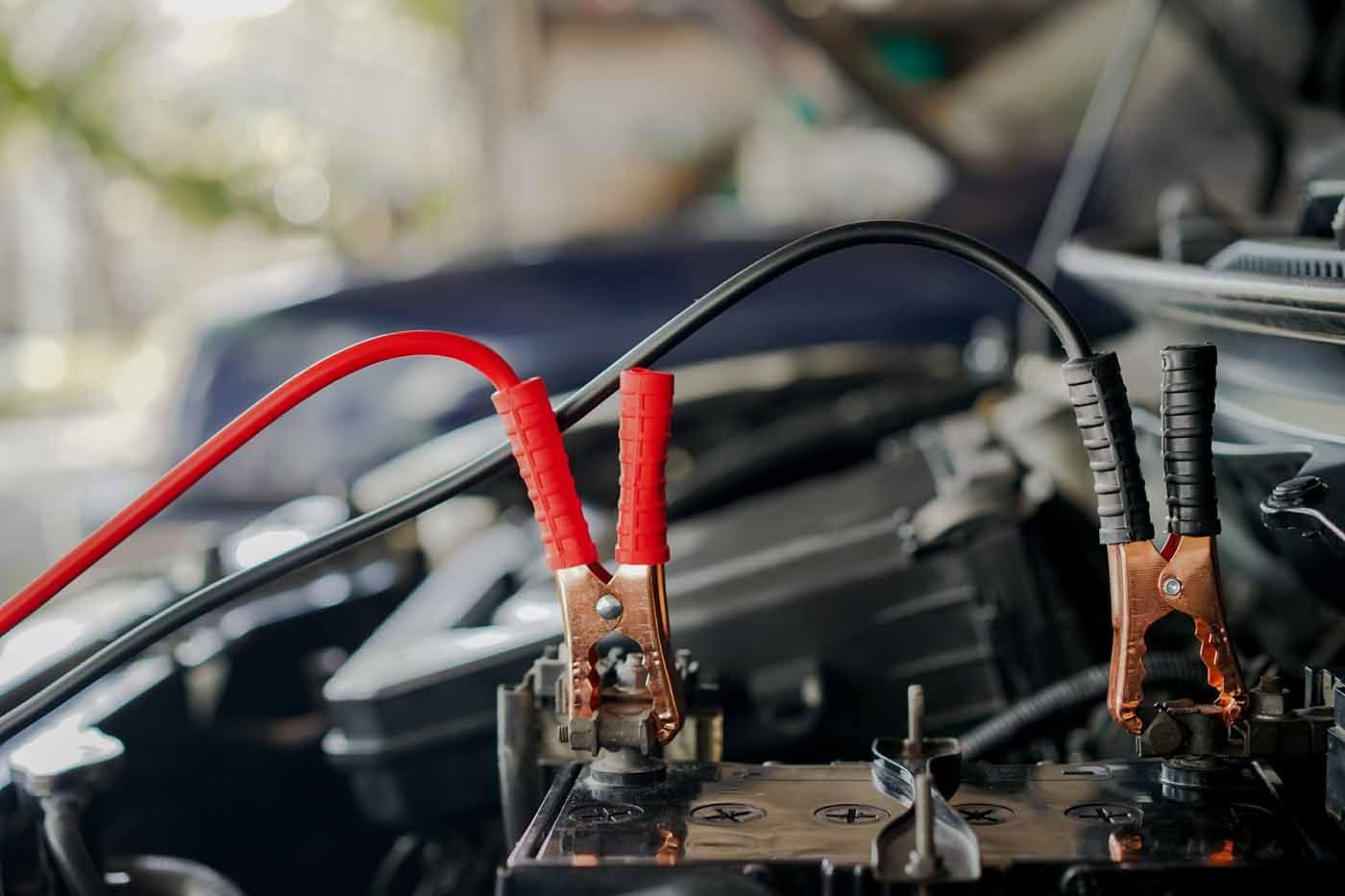 A close up of a car battery being charged with jumper cables.