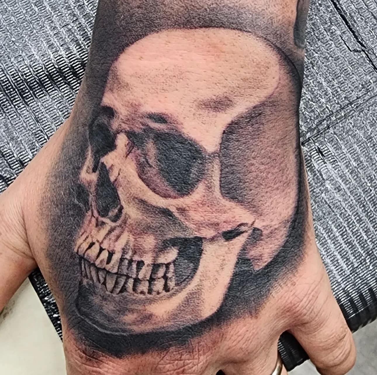 Realistic skull tattoo on the back of a hand, in black and gray tones