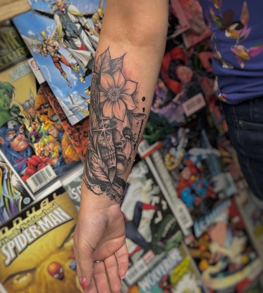 Forearm with detailed black floral tattoo, against a colorful comic book wall display.