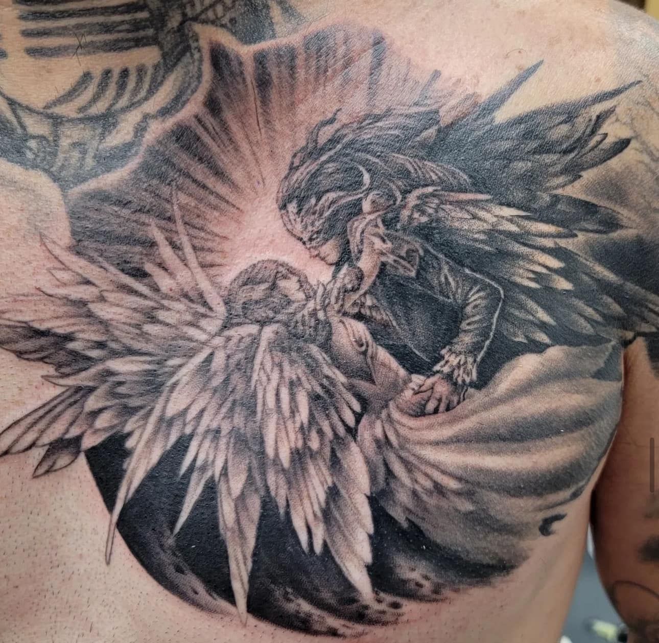 Black and gray tattoo of a winged figure and dragon on a person’s back