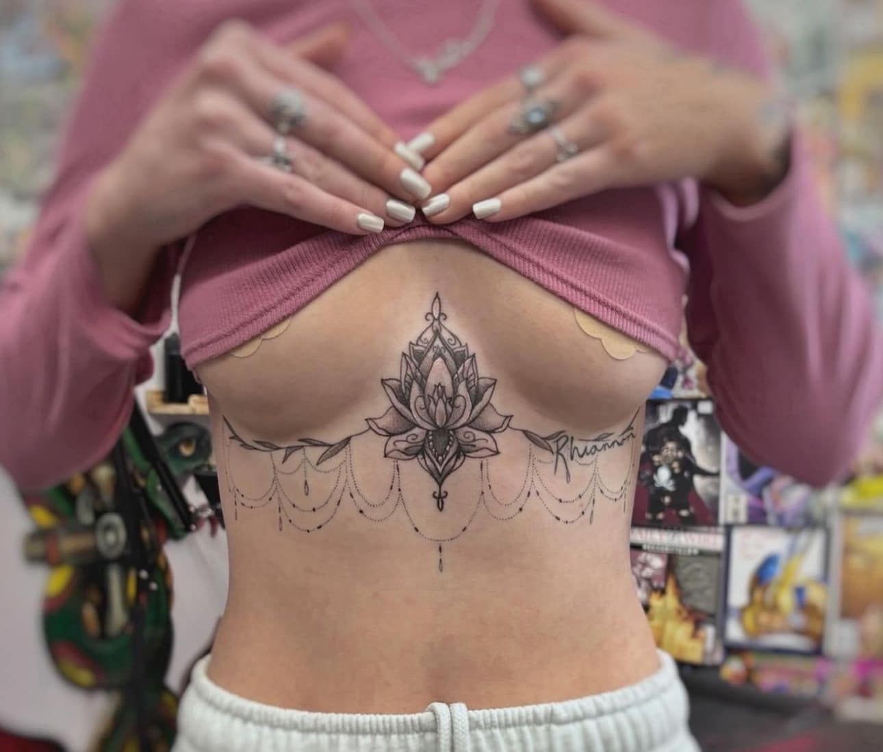 Torso with floral underboob tattoo and dangling chain design, hands lifting pink top