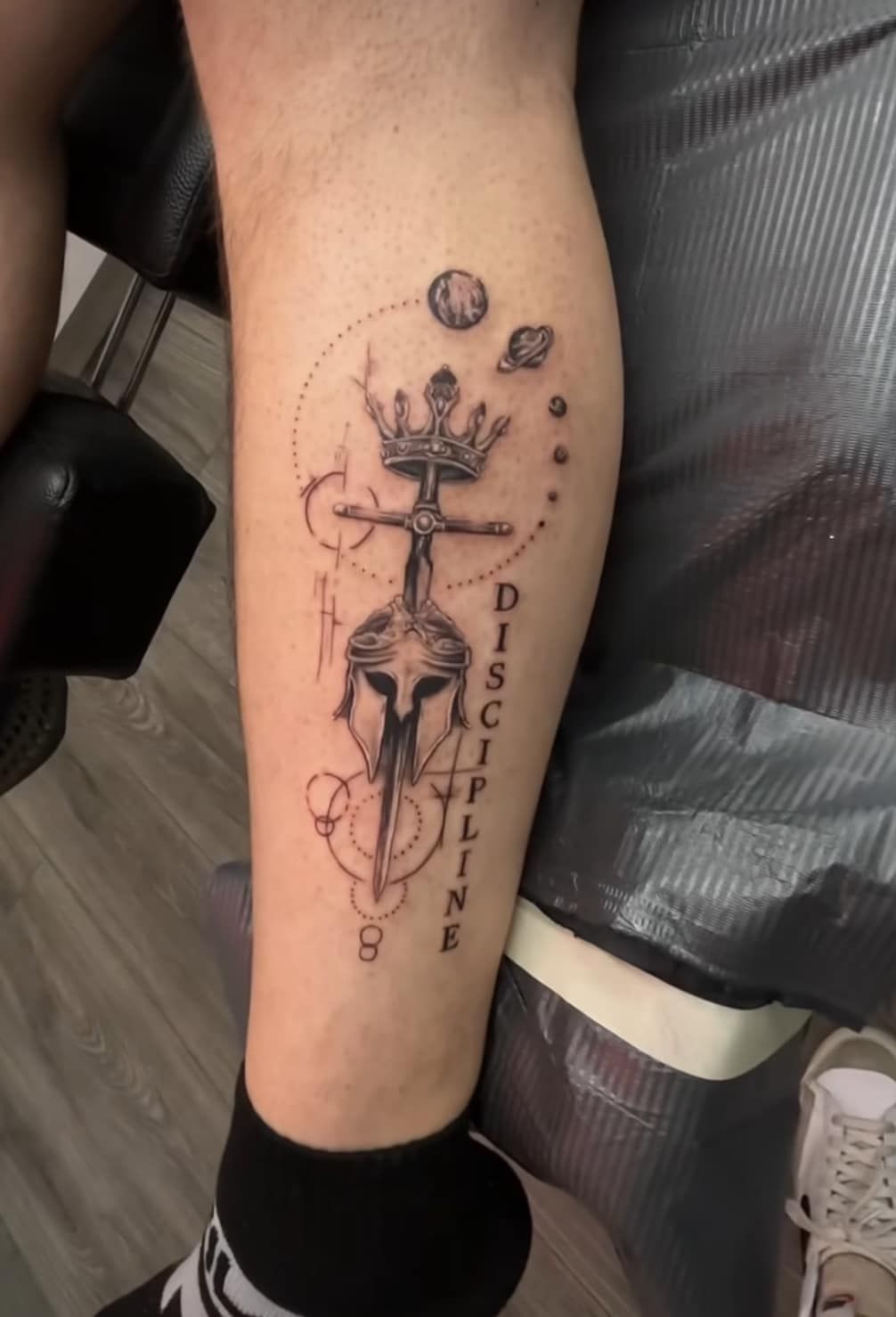 Close-up of a leg with a black tattoo of a crucifix and skull, with the word “DISCIPLE” beside it.