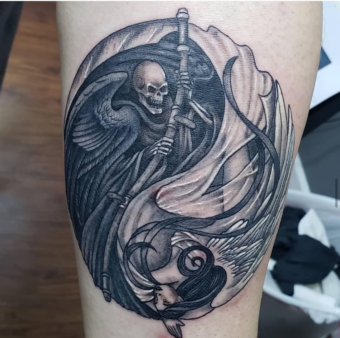 Black-and-gray tattoo of a hooded skeleton holding a scythe with swirling smoke-like ribbons