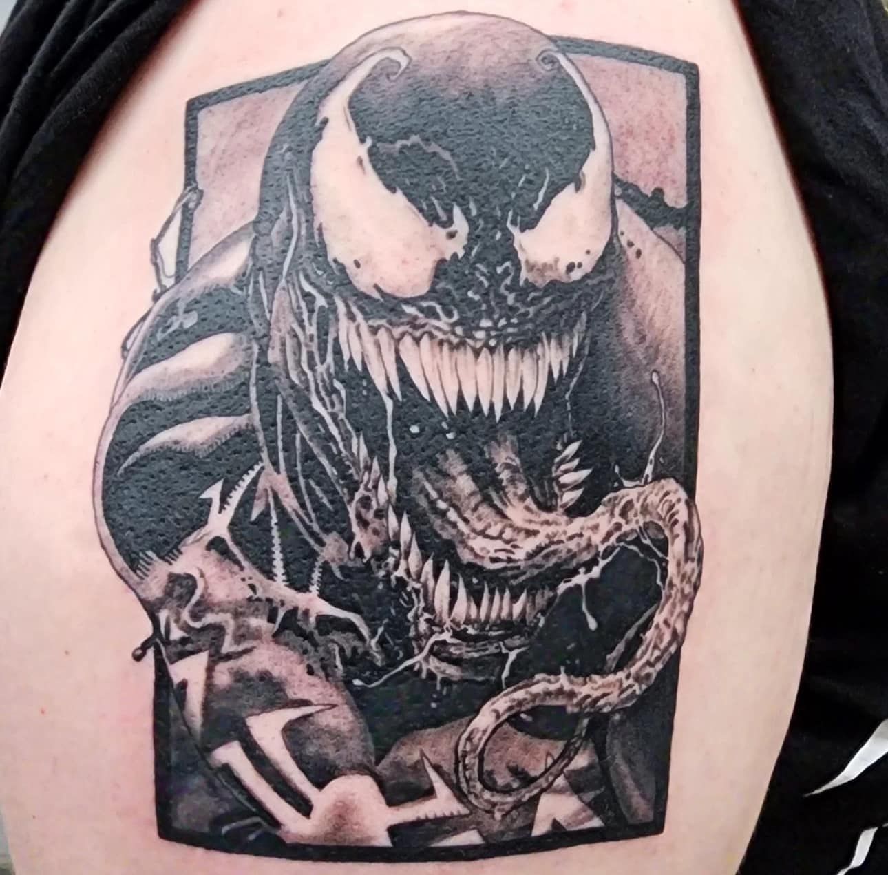 Black-and-gray Venom tattoo on an upper arm, showing the character snarling with sharp teeth.