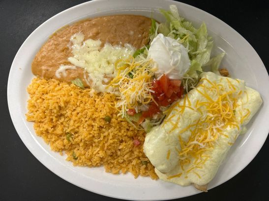 A white plate topped with rice , beans , cheese , lettuce and tomatoes.