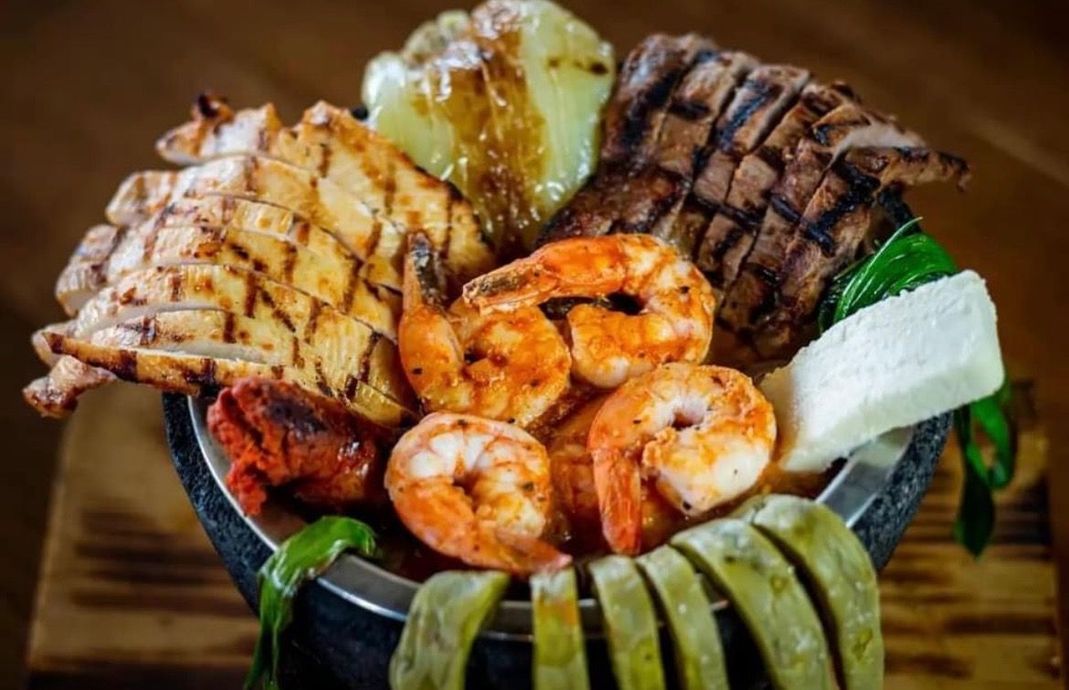 A bowl filled with shrimp , meat , and vegetables on a wooden table.