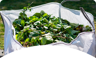 White bag filled with green leaves and branches in a yard.
