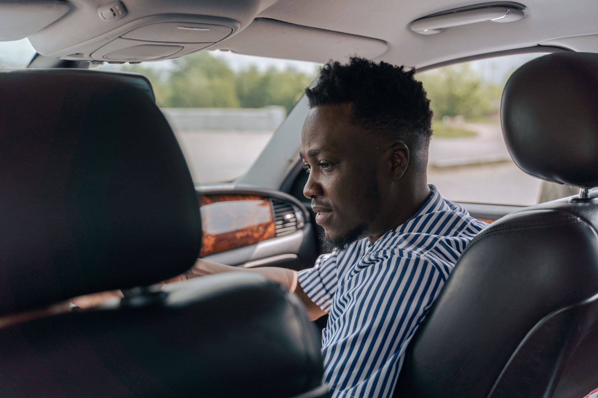 Person sitting in the back seat of a car, looking down, wearing a striped shirt