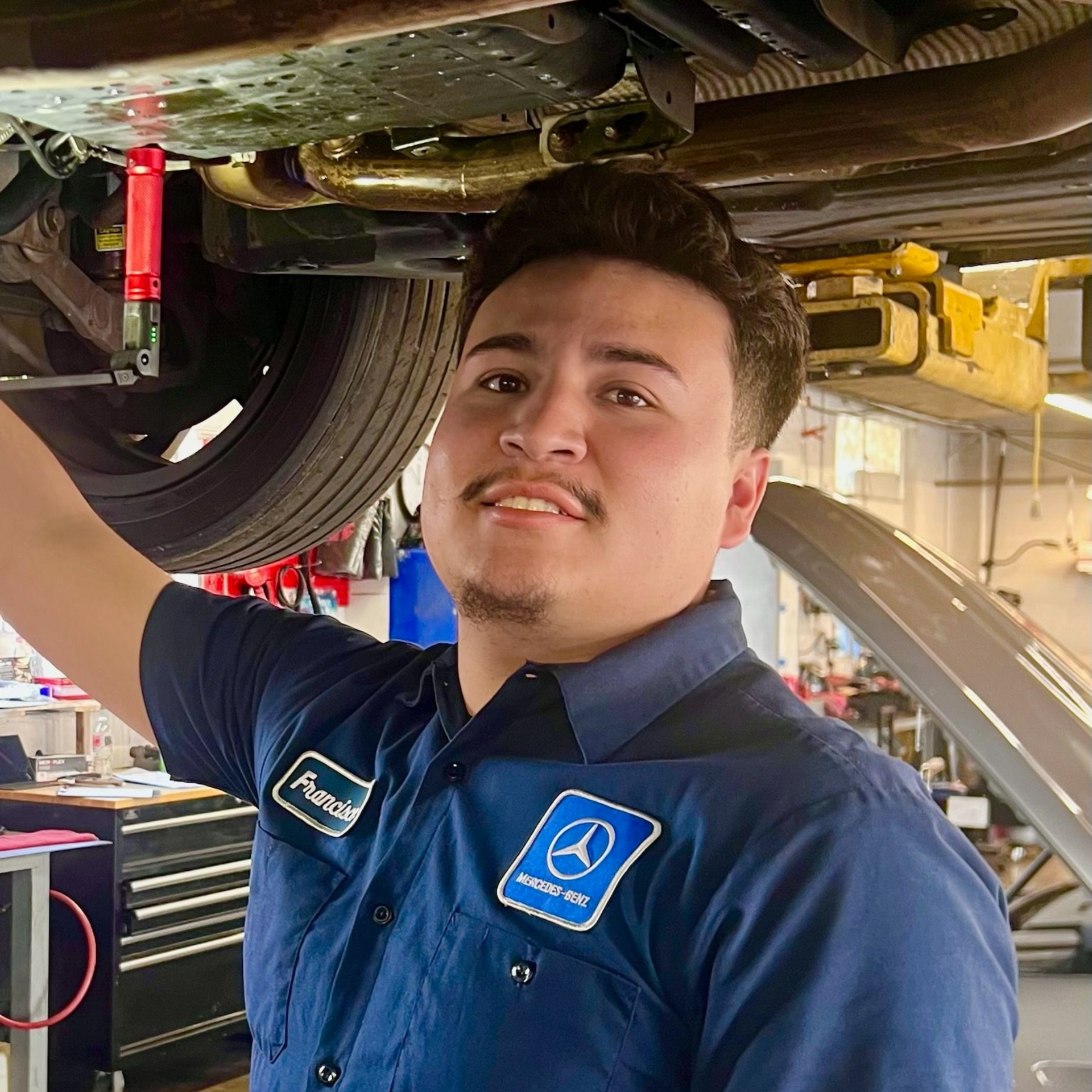 Mechanic working under a car, wearing a blue uniform.