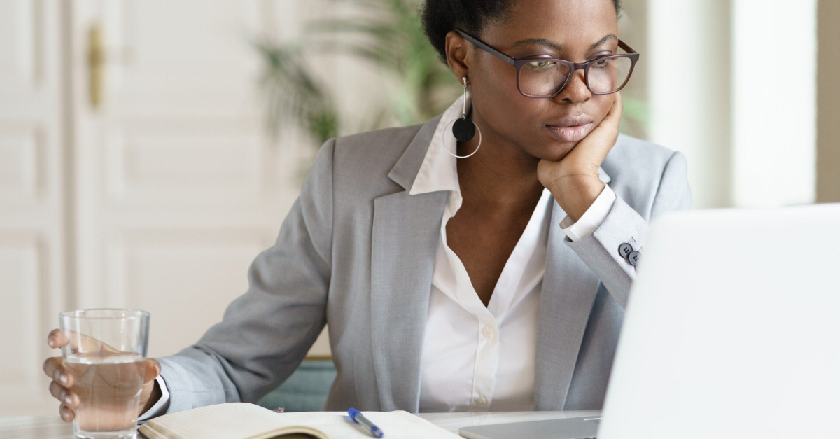 Focused young African American businesswoman in blazer working at laptop