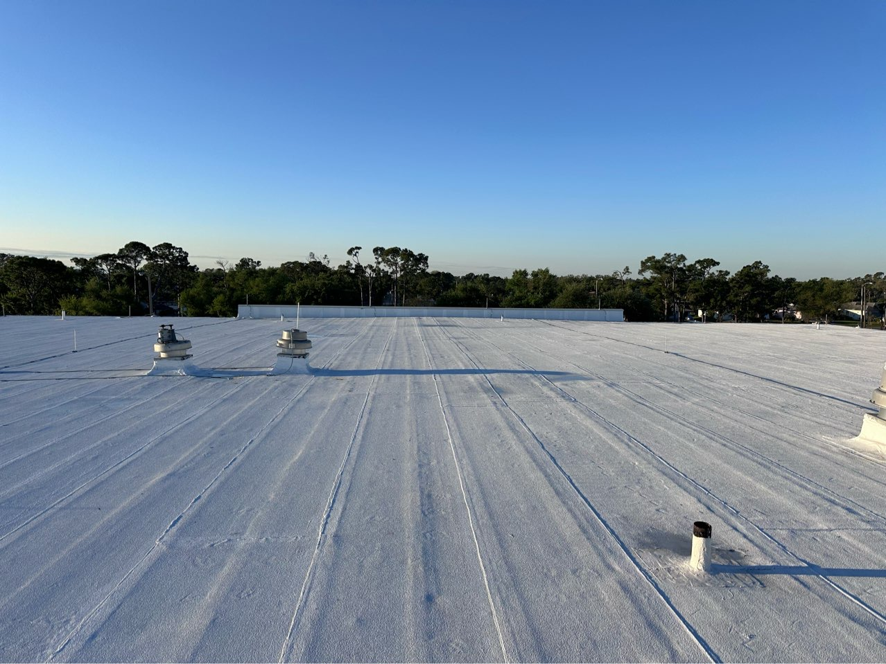 A white, flat roof under a clear blue sky, featuring several vents and a low perimeter wall.