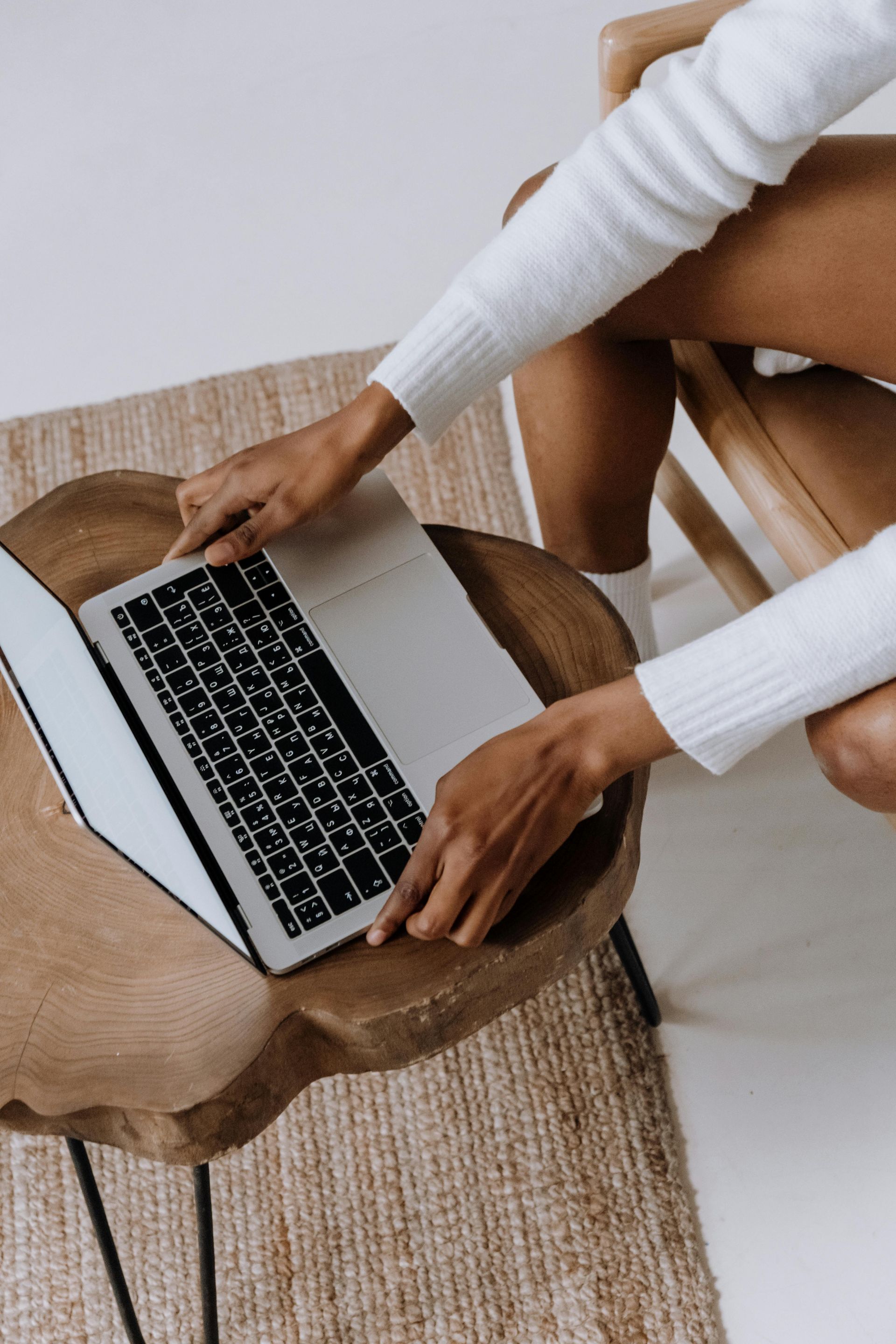 Person using a laptop on a wooden table, wearing a white sweater.