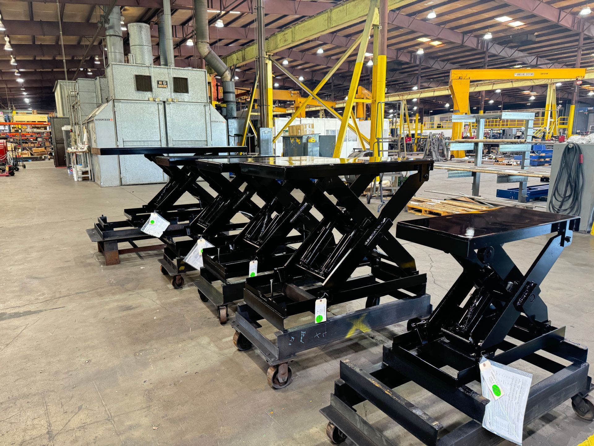 A row of scissor lifts are sitting on carts in Autoquip's warehouse