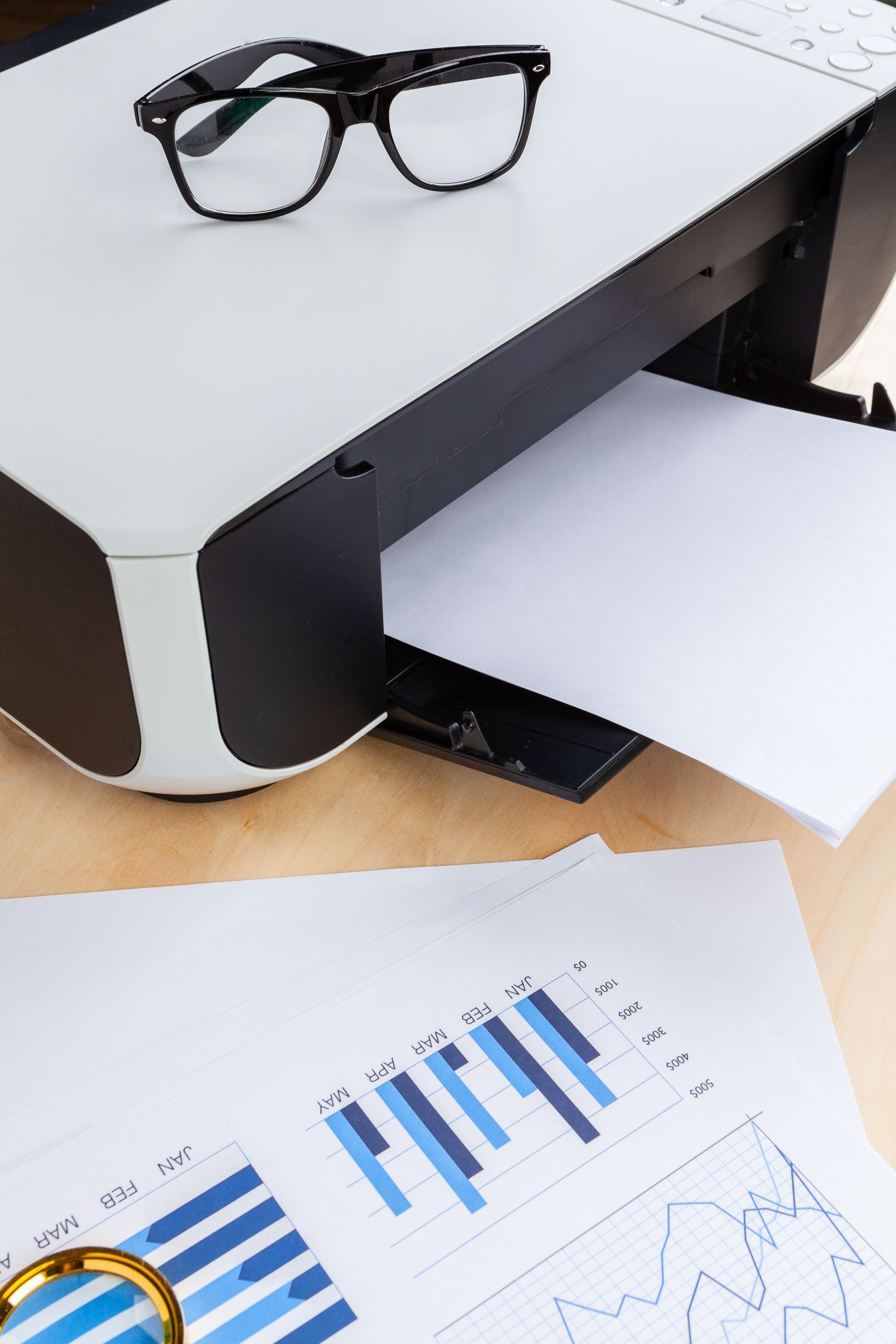A printer is sitting on a table next to a pair of glasses.