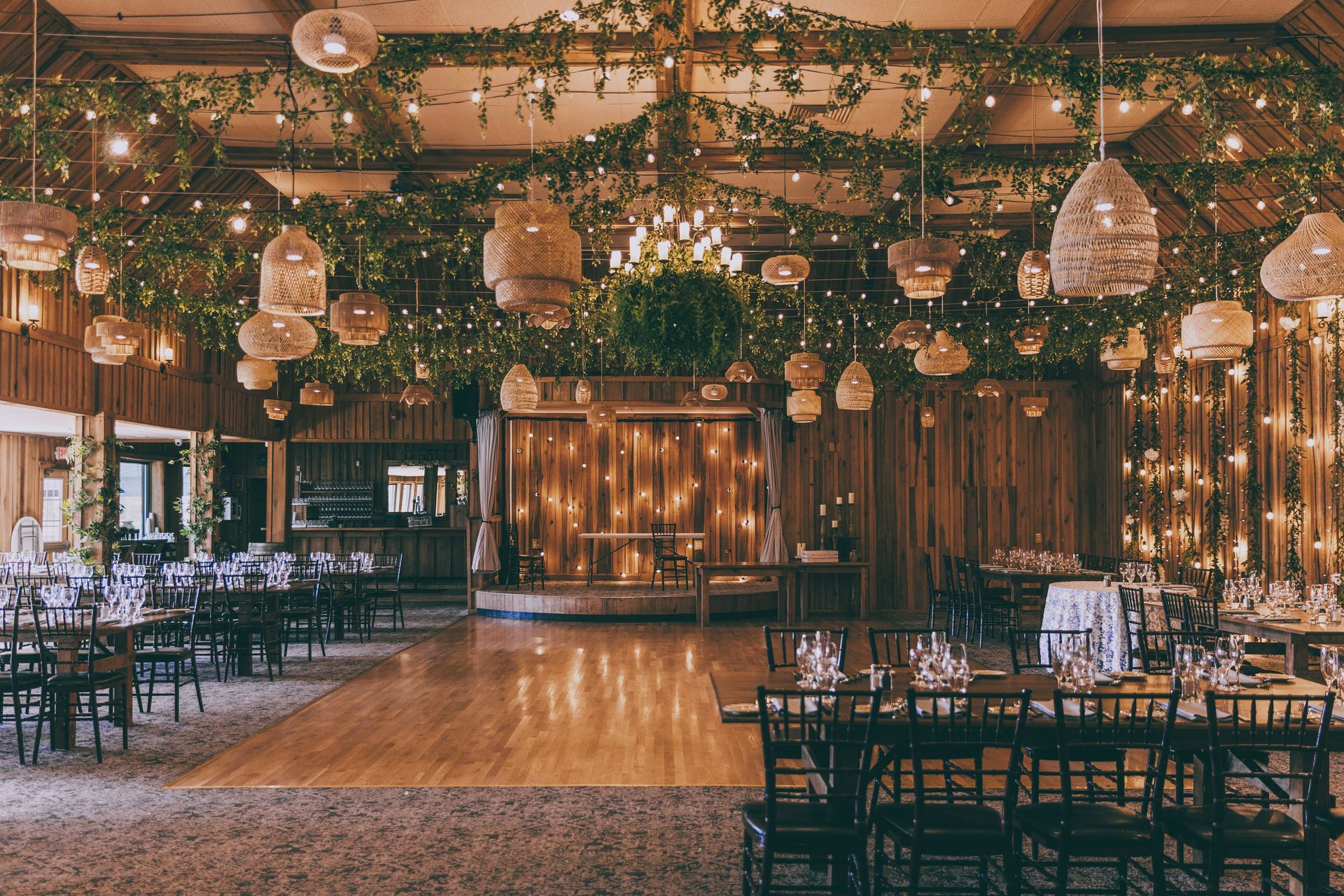 Natural colored hanging lights and dimly light greenery suspended from a ceiling in a wedding venue