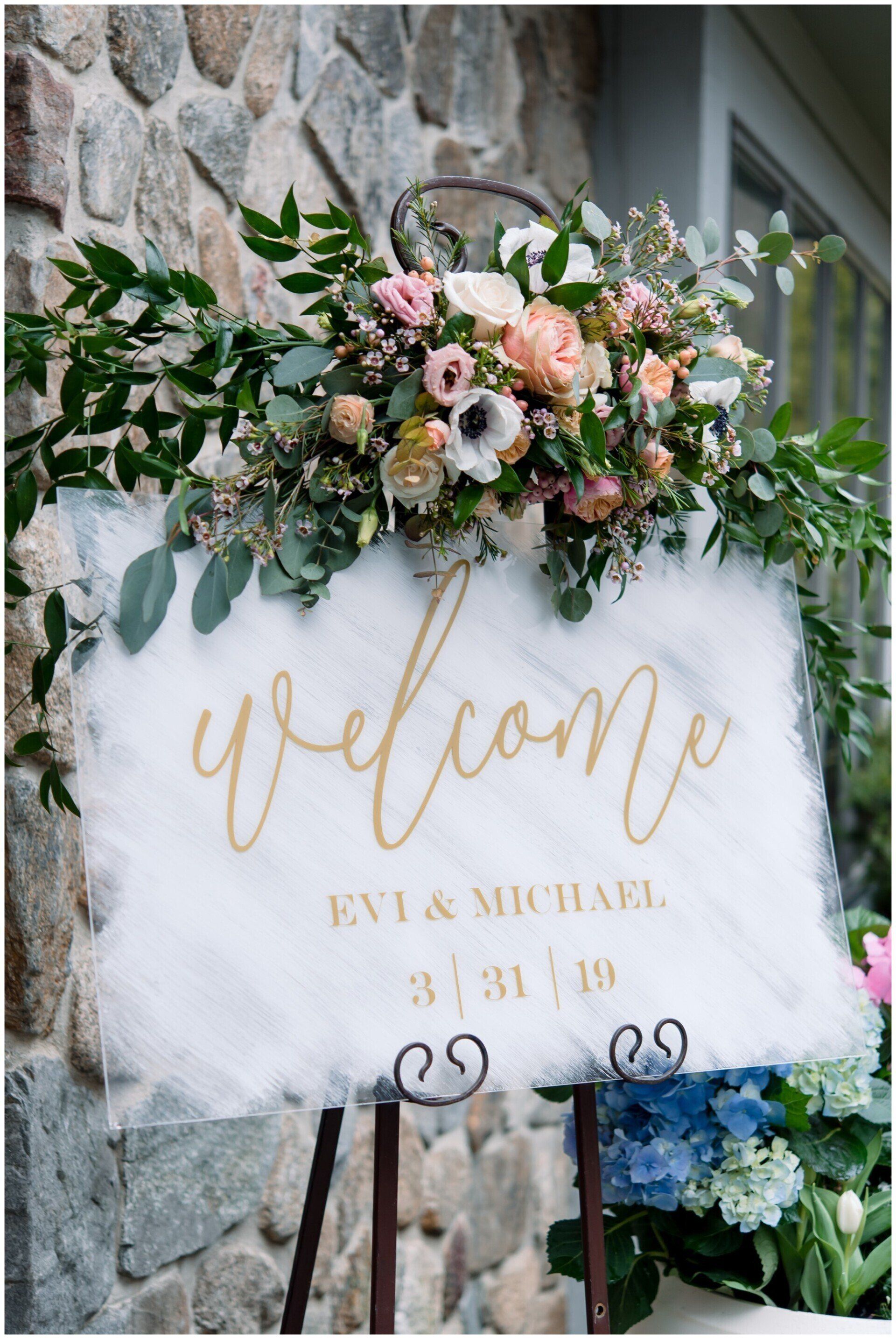 bridal welcome sign with gold text and flowers on top