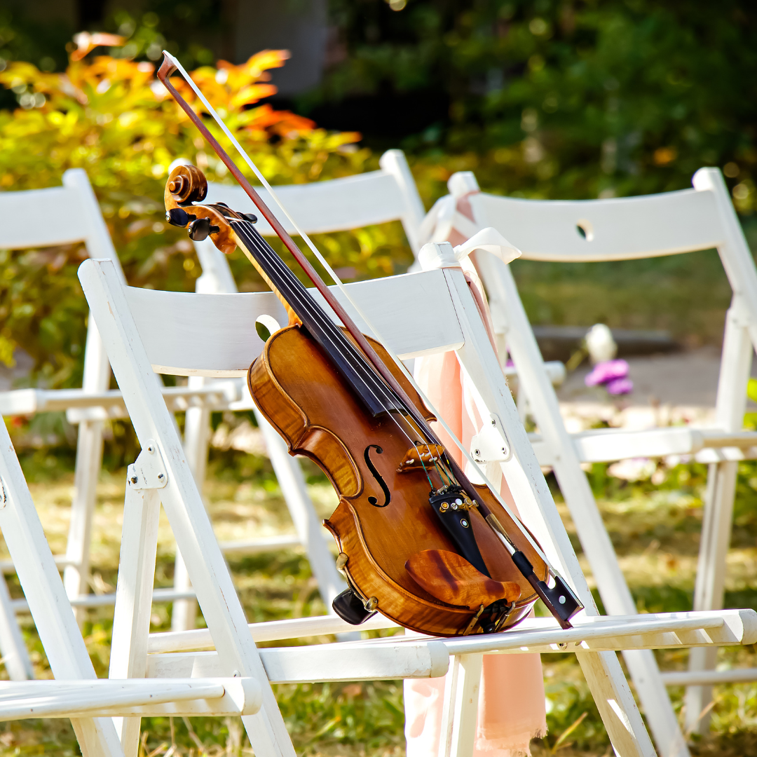 Violin resting on white chairs outdoors in a sunny garden setting