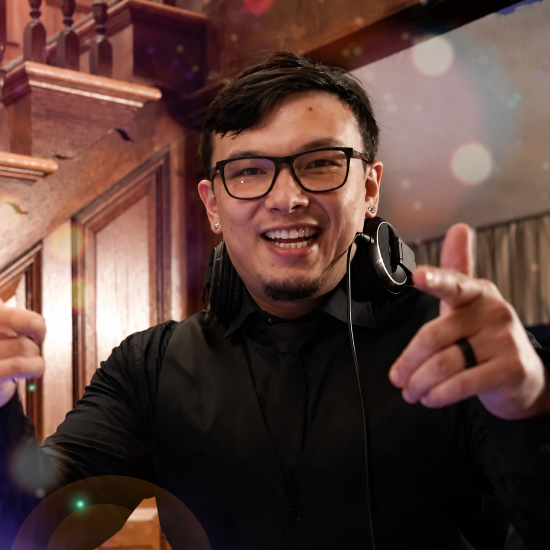 Smiling man in black shirt and glasses pointing at the camera in a warmly lit room