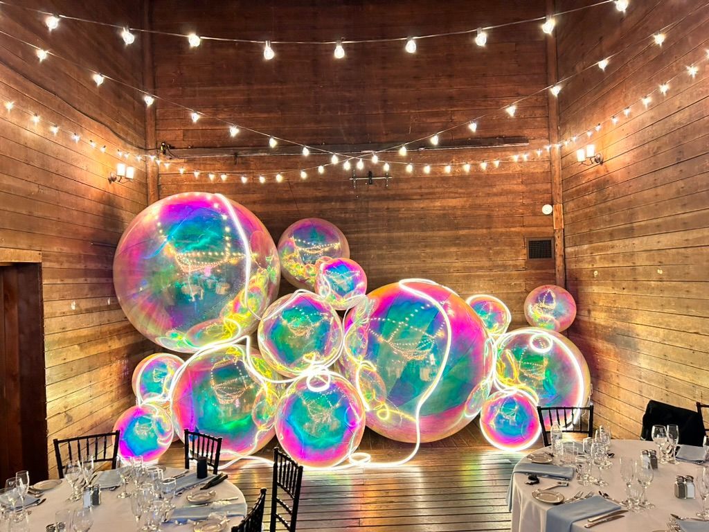 A event space with tables and chairs and a wall of lighted bubbles.