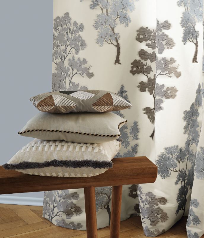 Ein Stapel Kissen liegt auf einer Holzbank vor Vorhängen mit Bäumen darauf