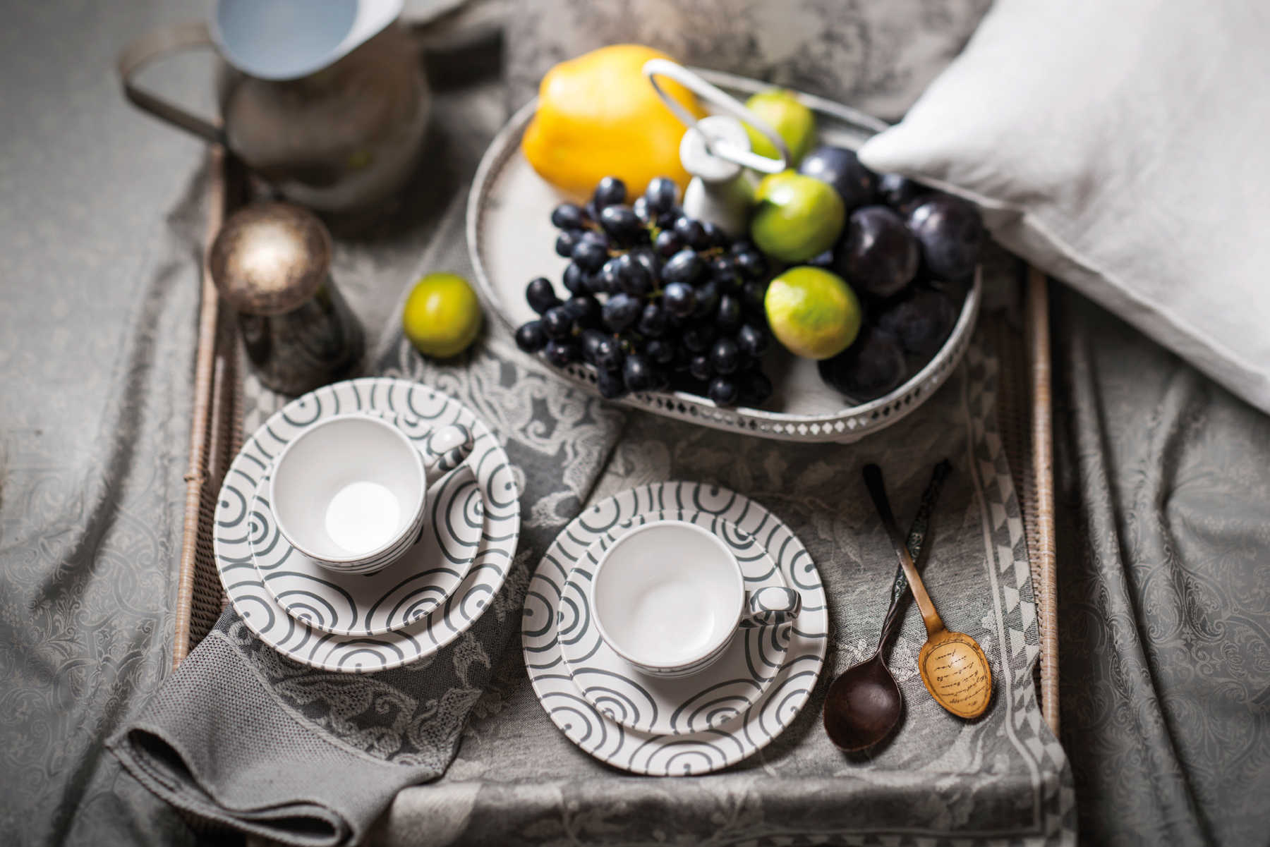 Ein Holztablett mit zwei Tassen und Untertassen, einer Obstschale und Löffeln.