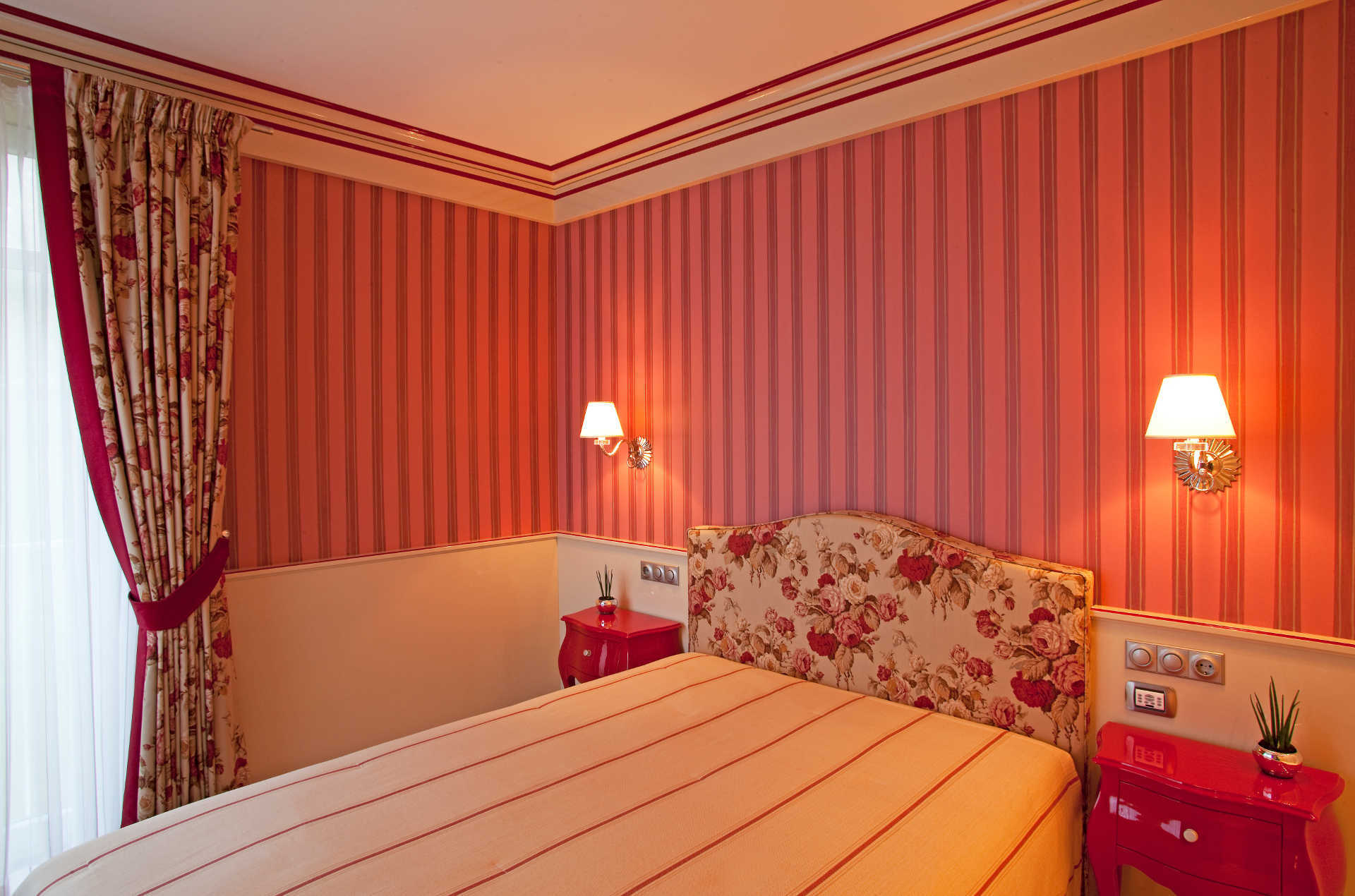 Ein Schlafzimmer mit rosa gestreiften Wänden und einem Bett mit geblümtem Kopfteil.