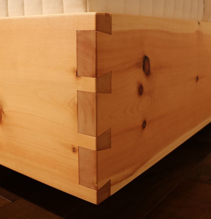 Eine Nahaufnahme von einem hölzernen Bettrahmen mit einer Matratze im Hintergrund