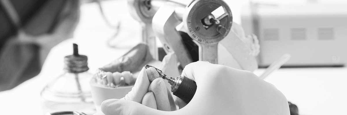 Eine behandschuhte Hand arbeitet in einer medizinischen Umgebung mit Instrumenten an einem Zahnmodell.