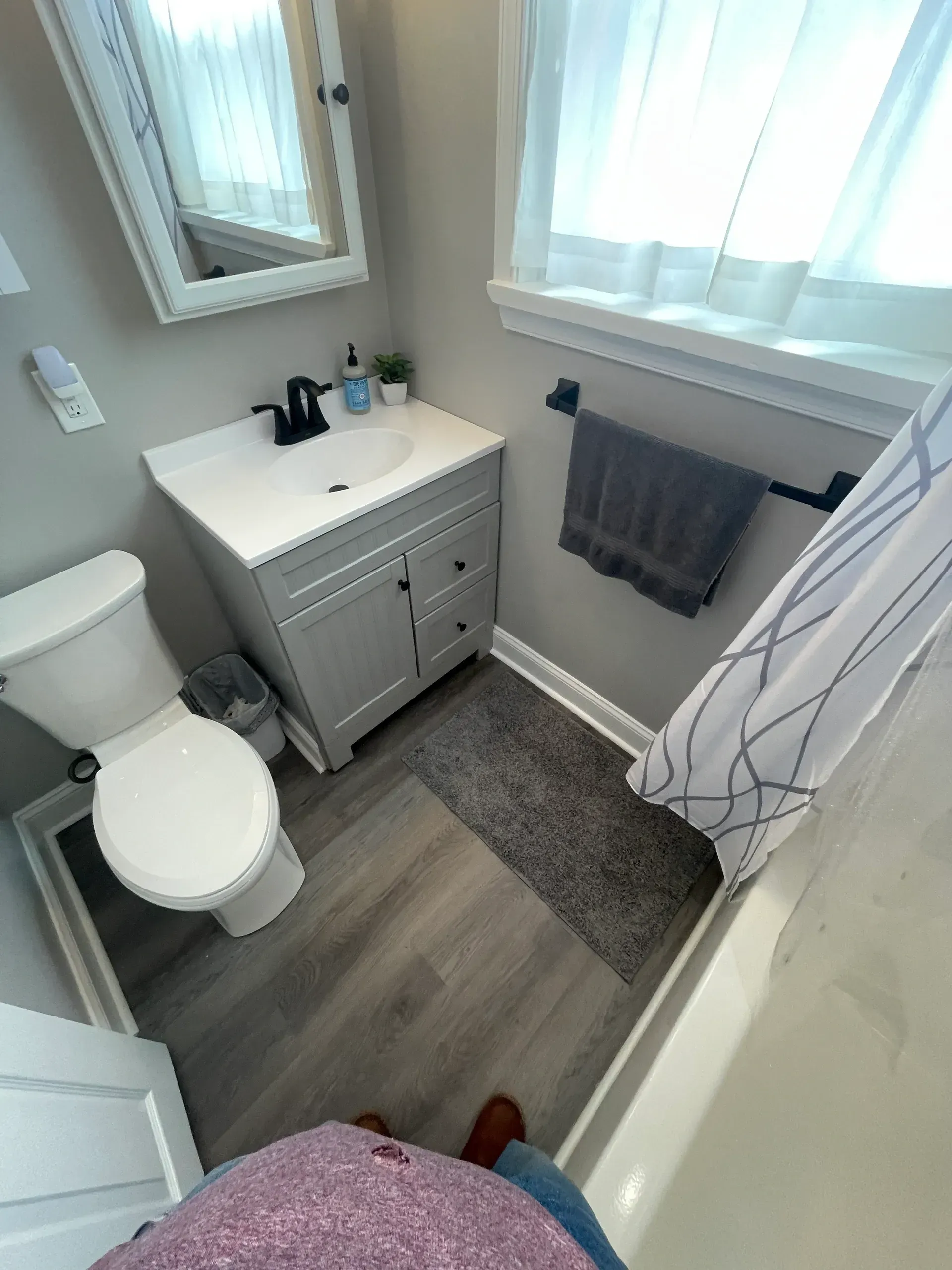 Small bathroom with gray vanity, toilet, tub, and window. Gray floor.