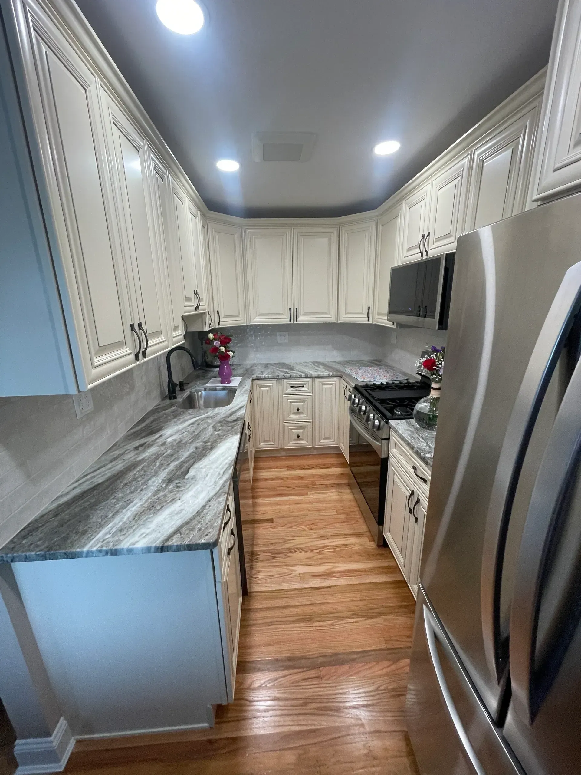 Cream-colored kitchen cabinets with gray countertops and stainless steel appliances. Hardwood floors.