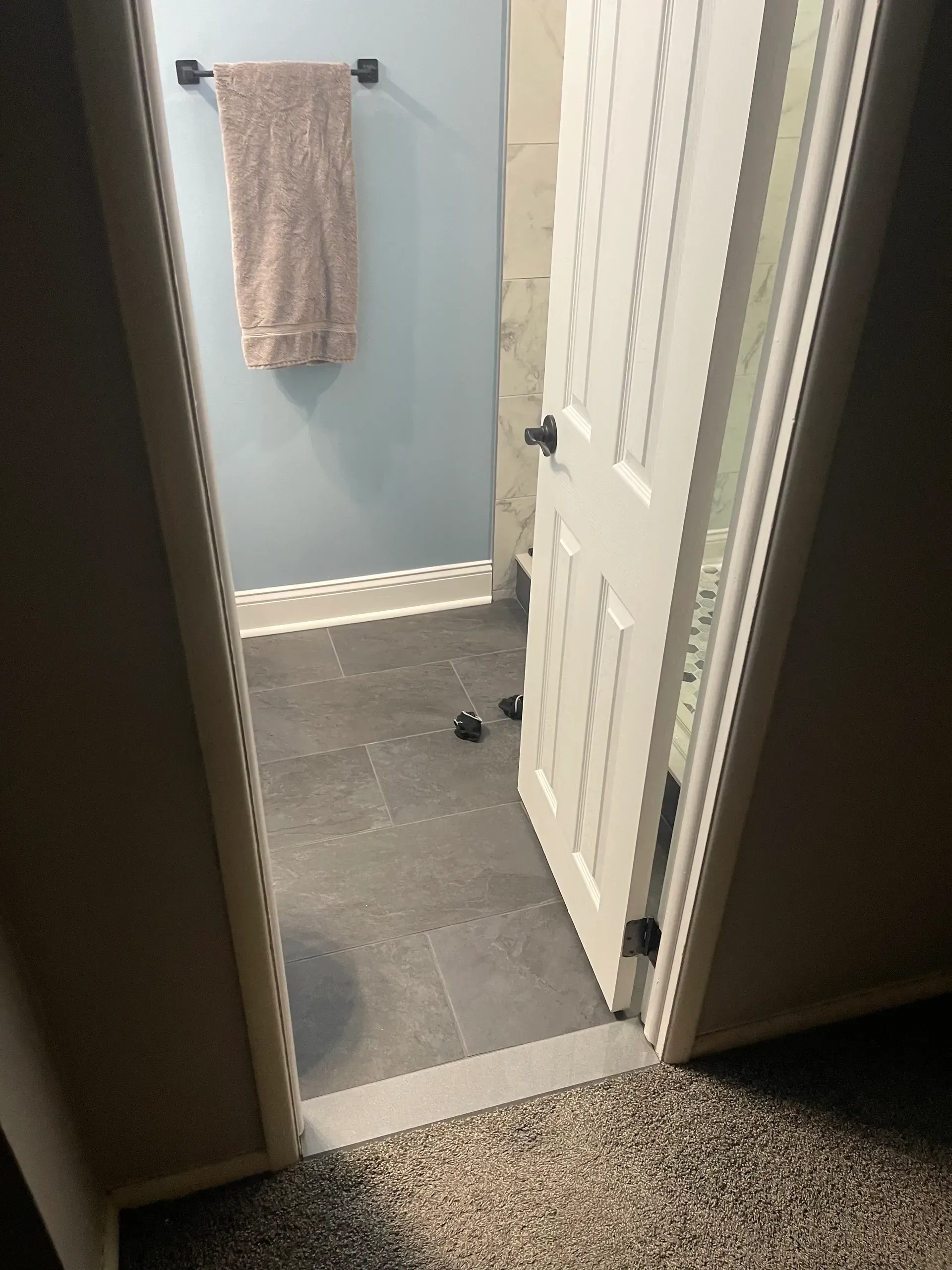 Bathroom doorway with open white door, towel bar, blue wall, dark floor.