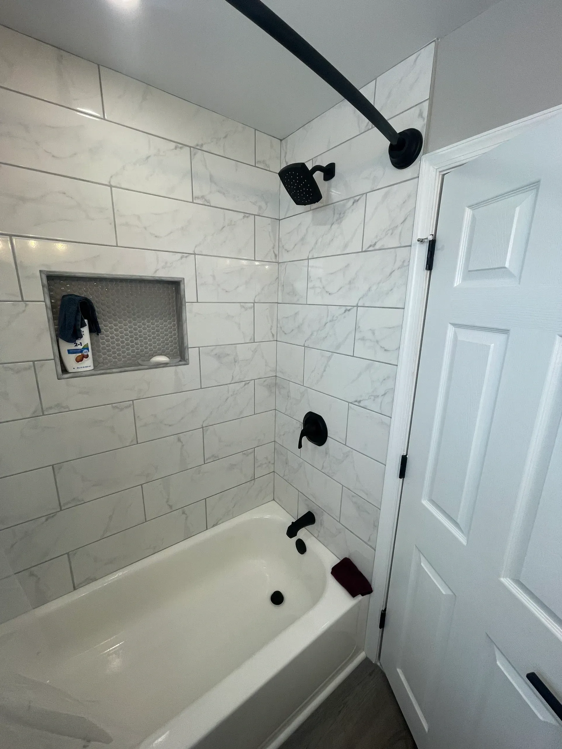 White-tiled bathroom with black fixtures, including a showerhead, faucet, and curtain rod, over a white bathtub.