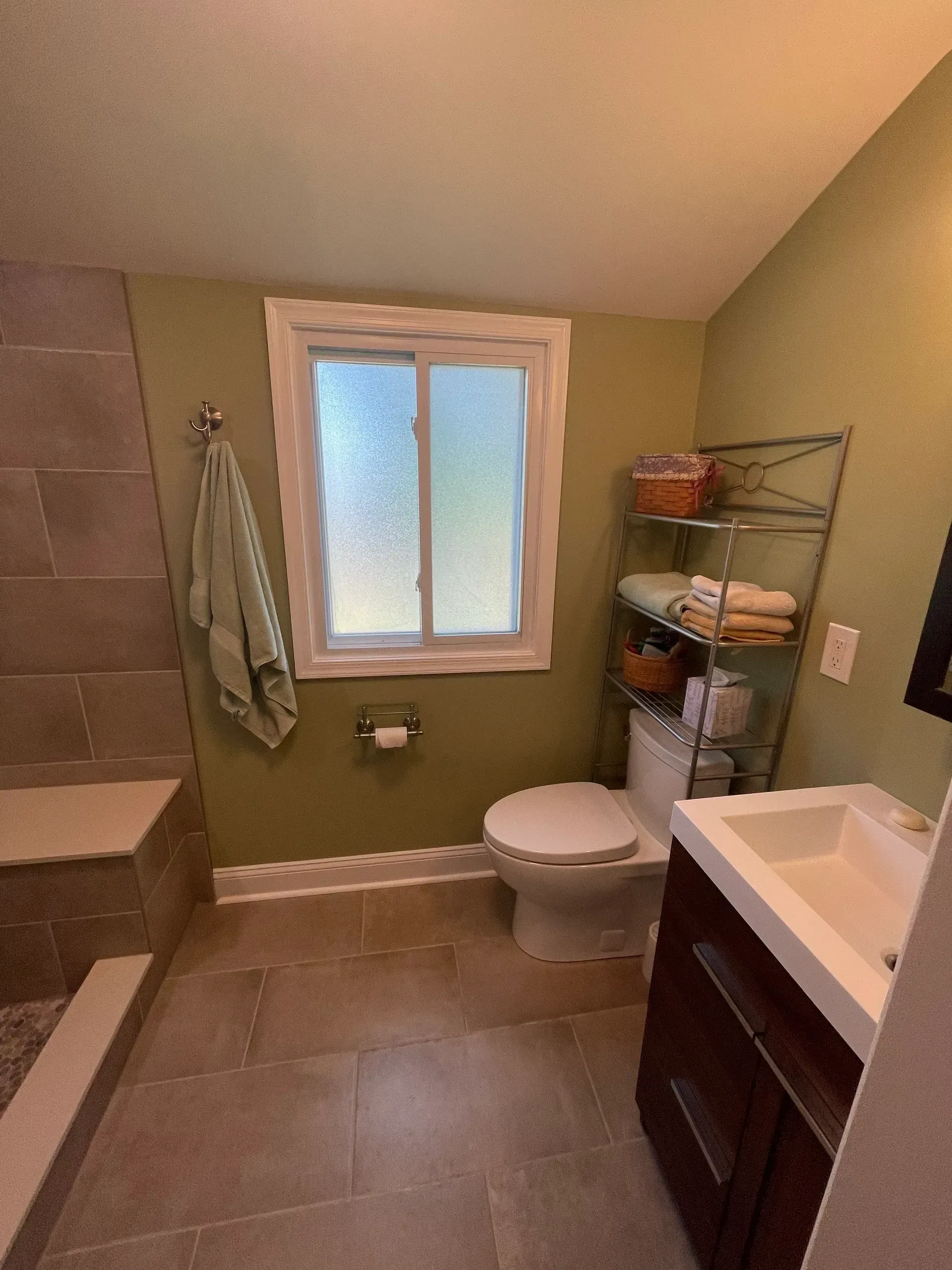Bathroom with green walls, tile floor, white toilet, and sink with dark cabinet.
