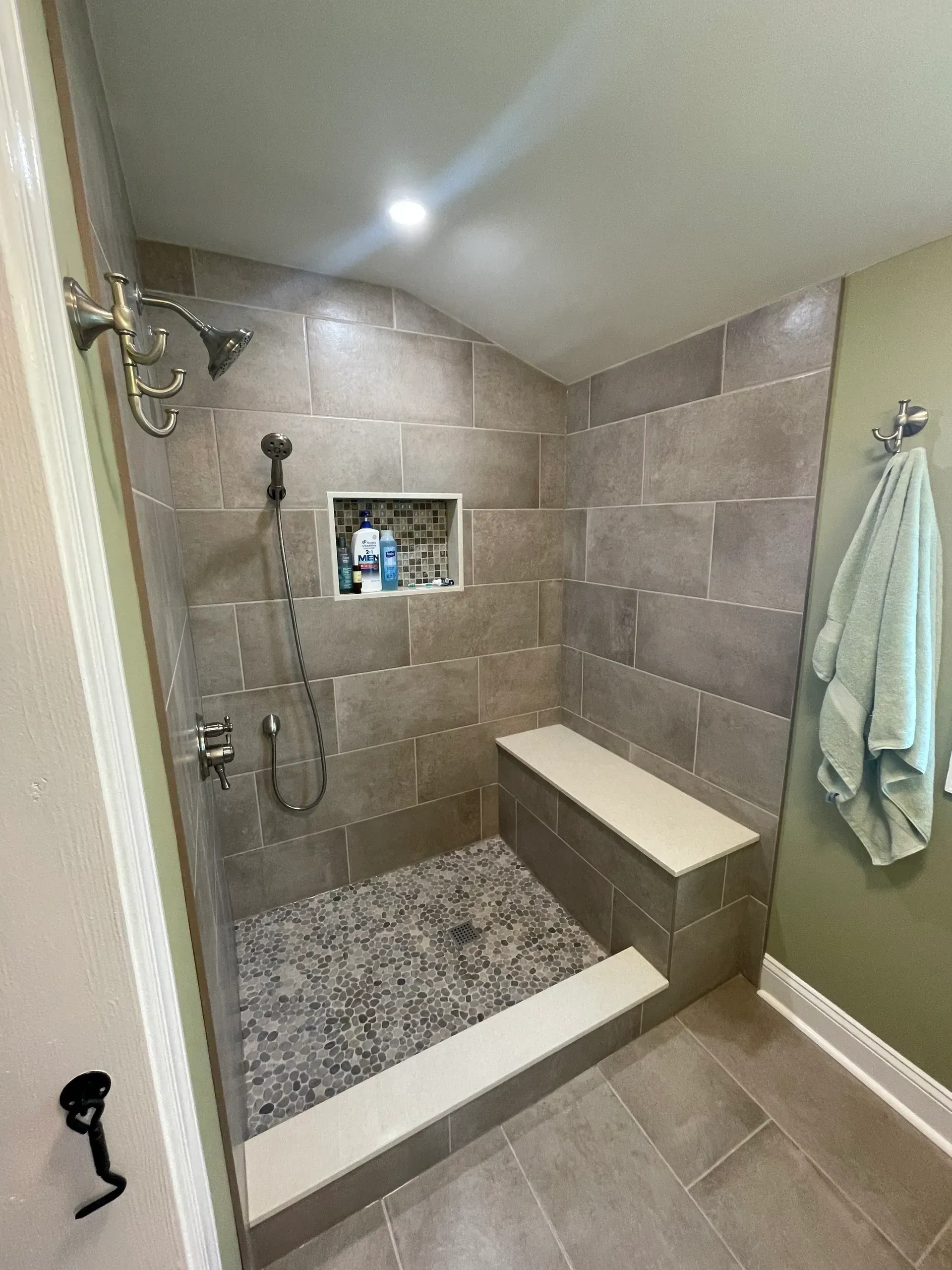 Shower with stone tile walls, built-in bench, pebble floor, and handheld showerhead.