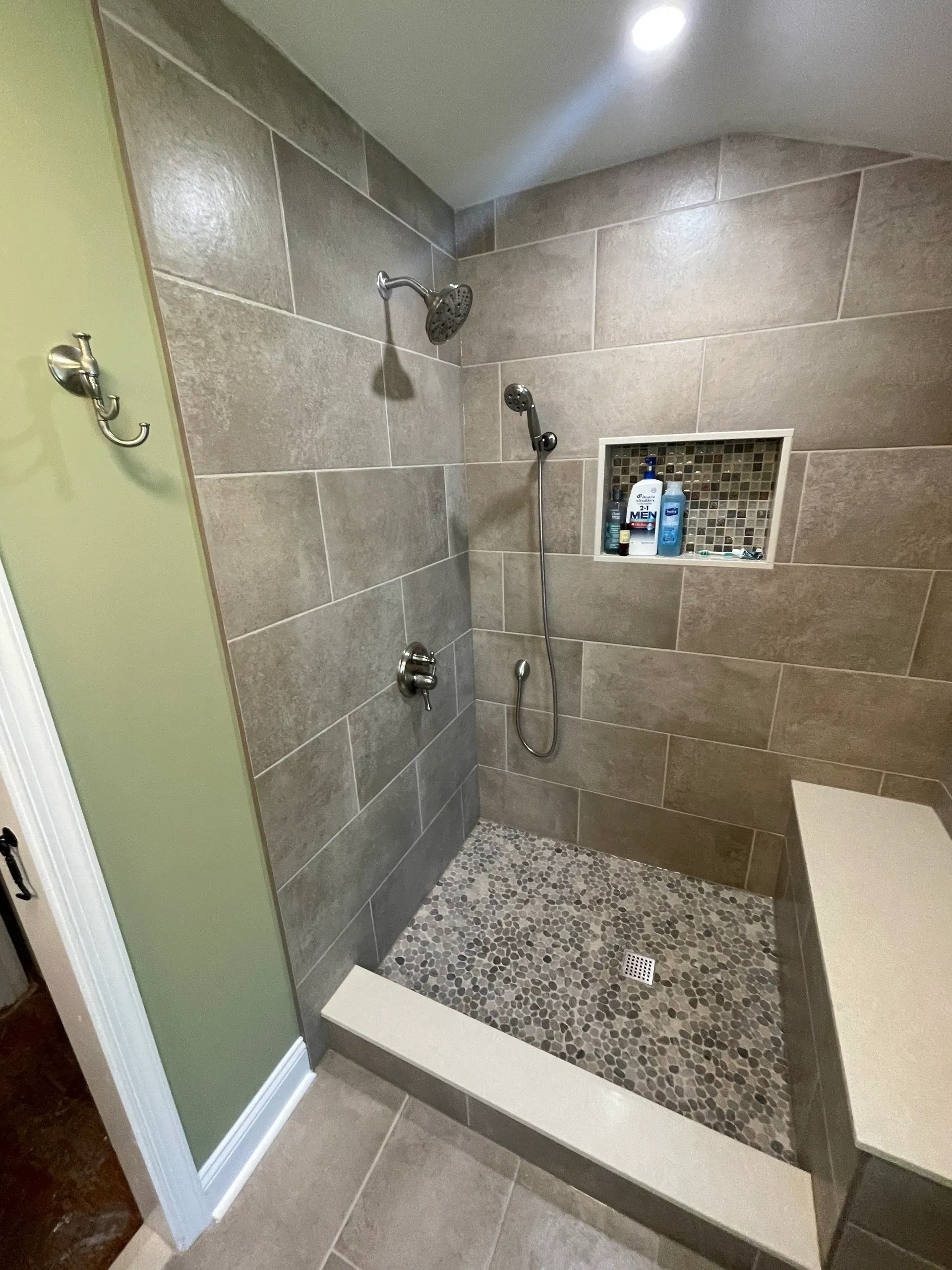Shower with gray tile walls, pebble floor, built-in bench, and a recessed shelf.