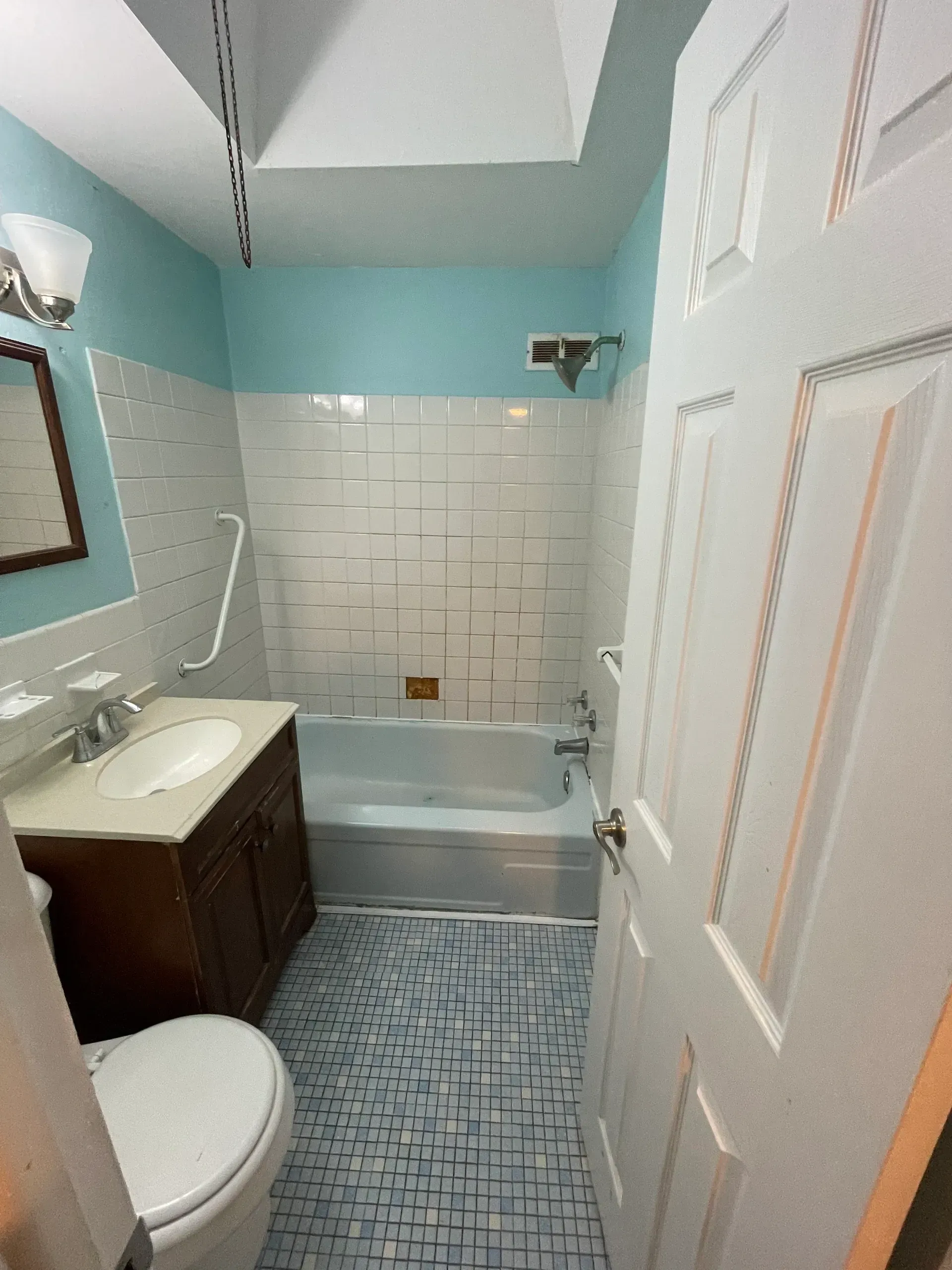 Bathroom with blue and white tile, dark wood vanity, white toilet, and open door.