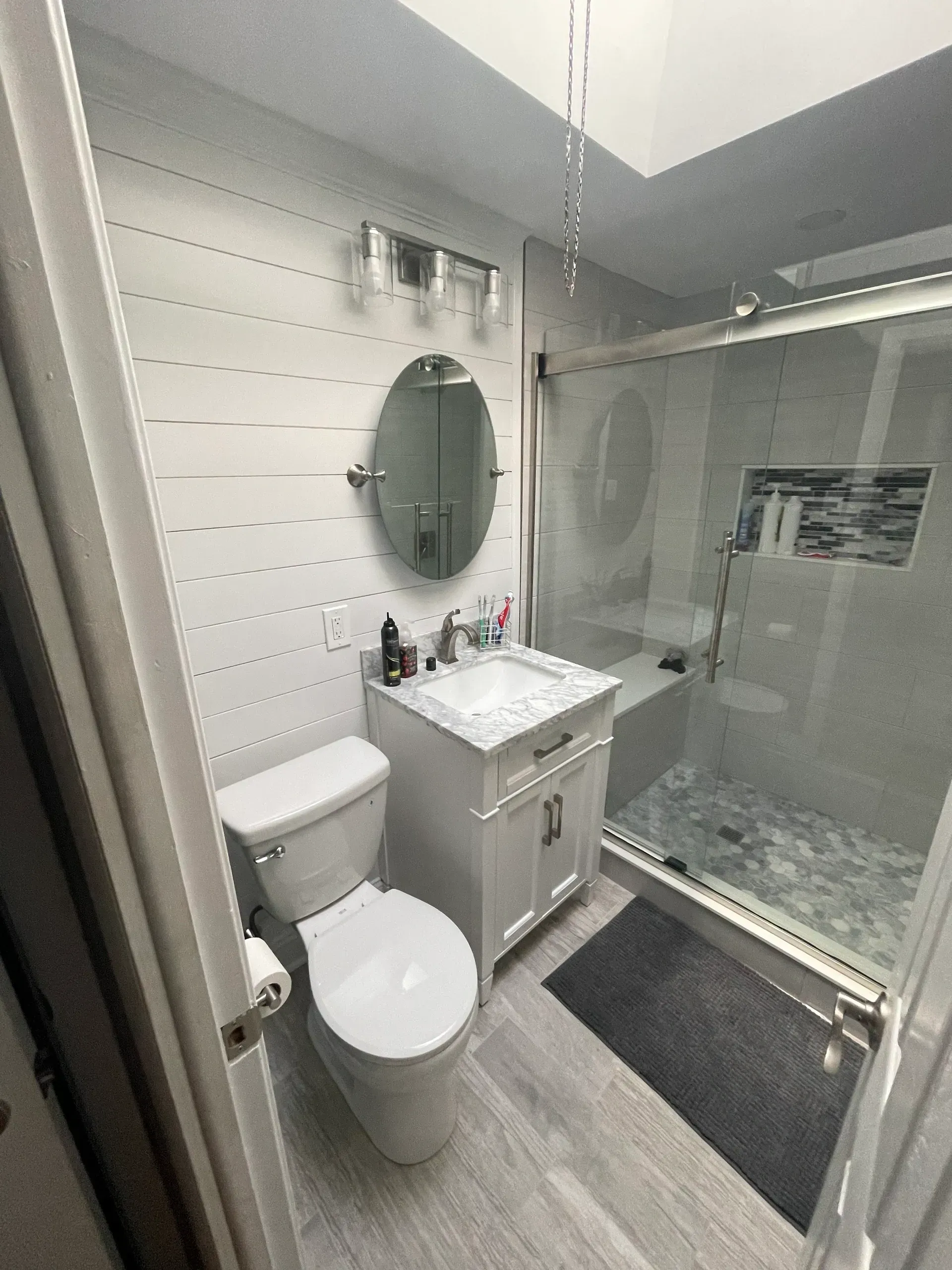 Modern white bathroom with toilet, vanity, and glass shower, gray floors and a skylight.