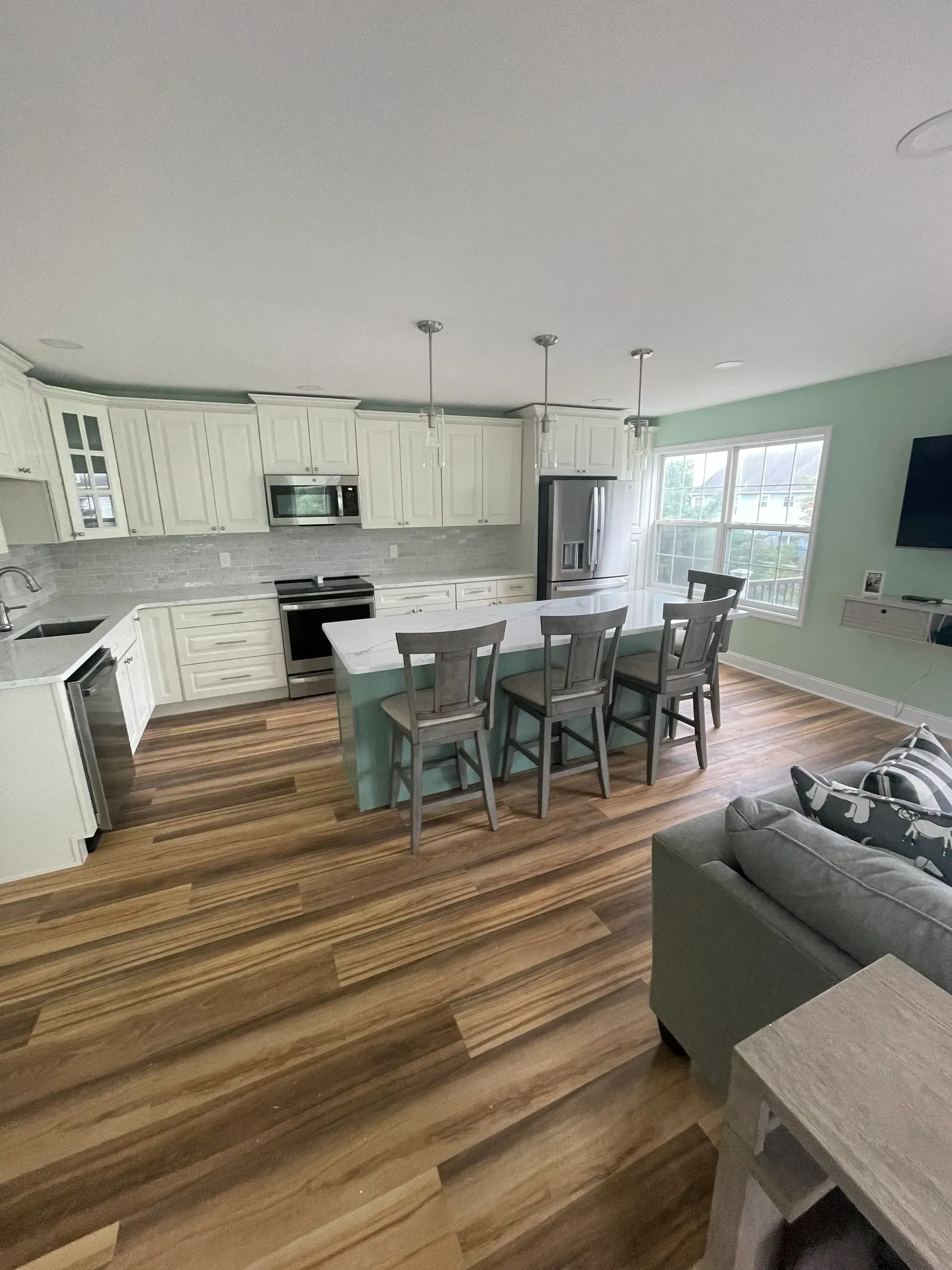 Kitchen with white cabinets, green island, and wood floors. Dining area with bar stools.
