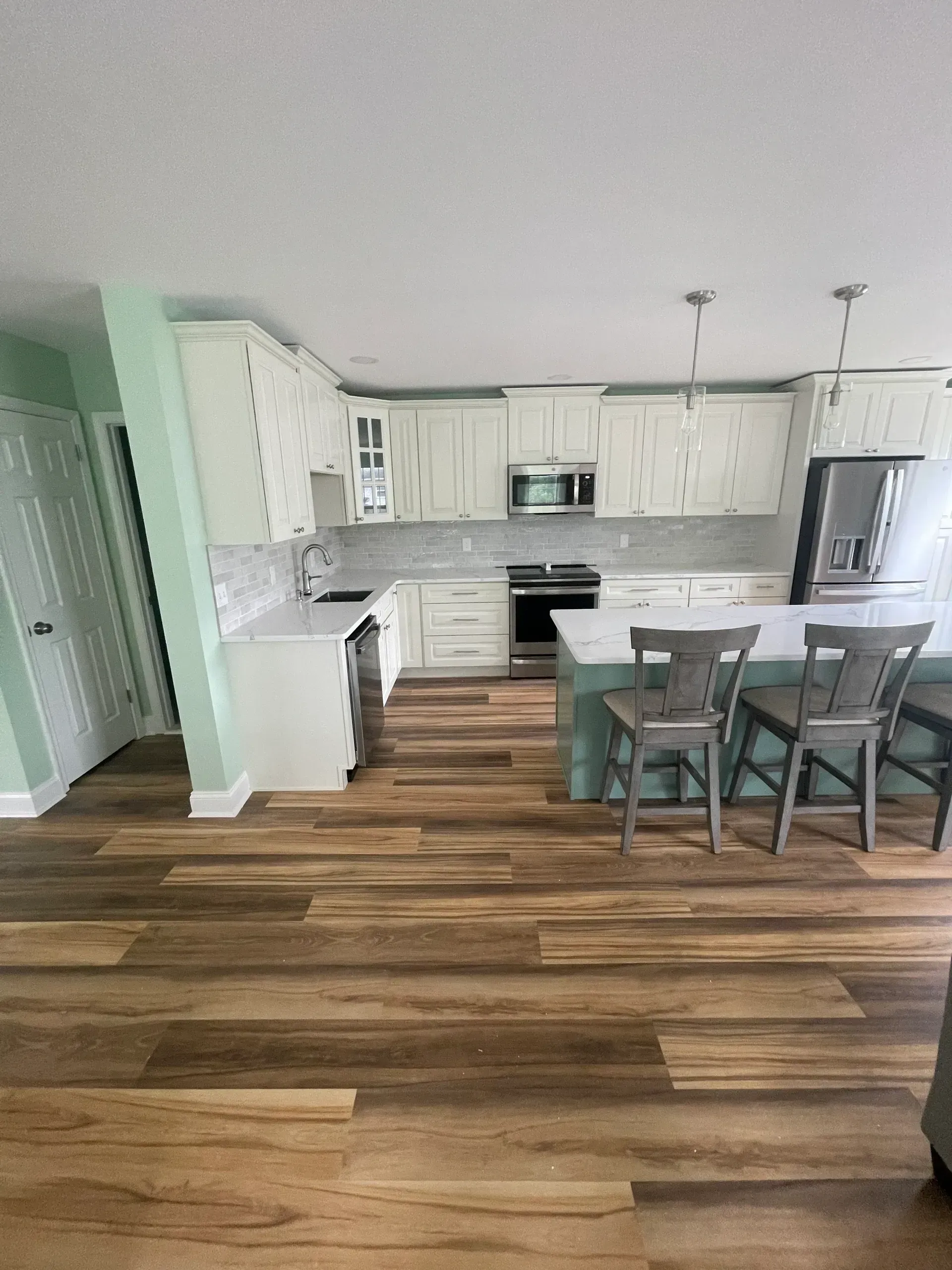 Kitchen with wood floors, white cabinets, island with green base, and gray stools.