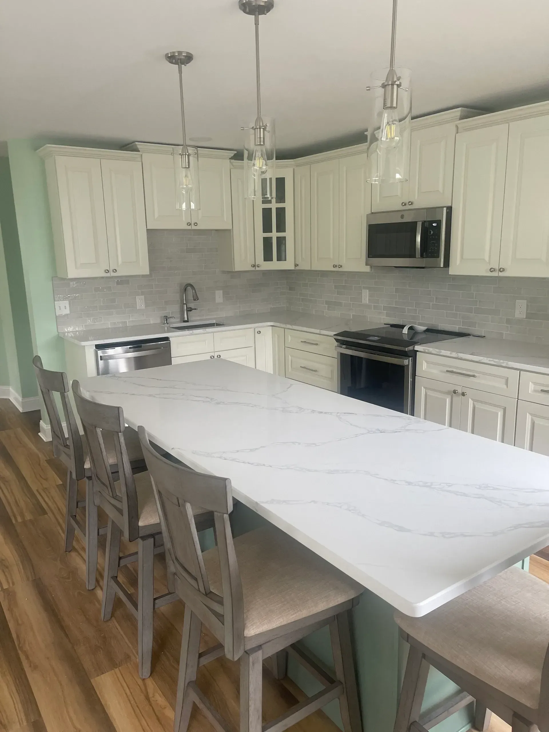 Kitchen with white cabinets, quartz countertop island, and light fixtures.
