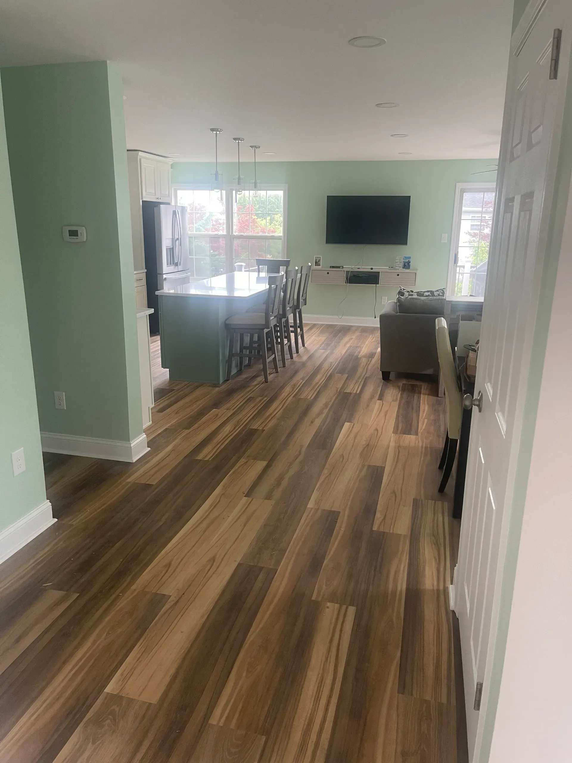 Open-concept interior with wood floors, green walls, kitchen island with stools, and living area with TV.