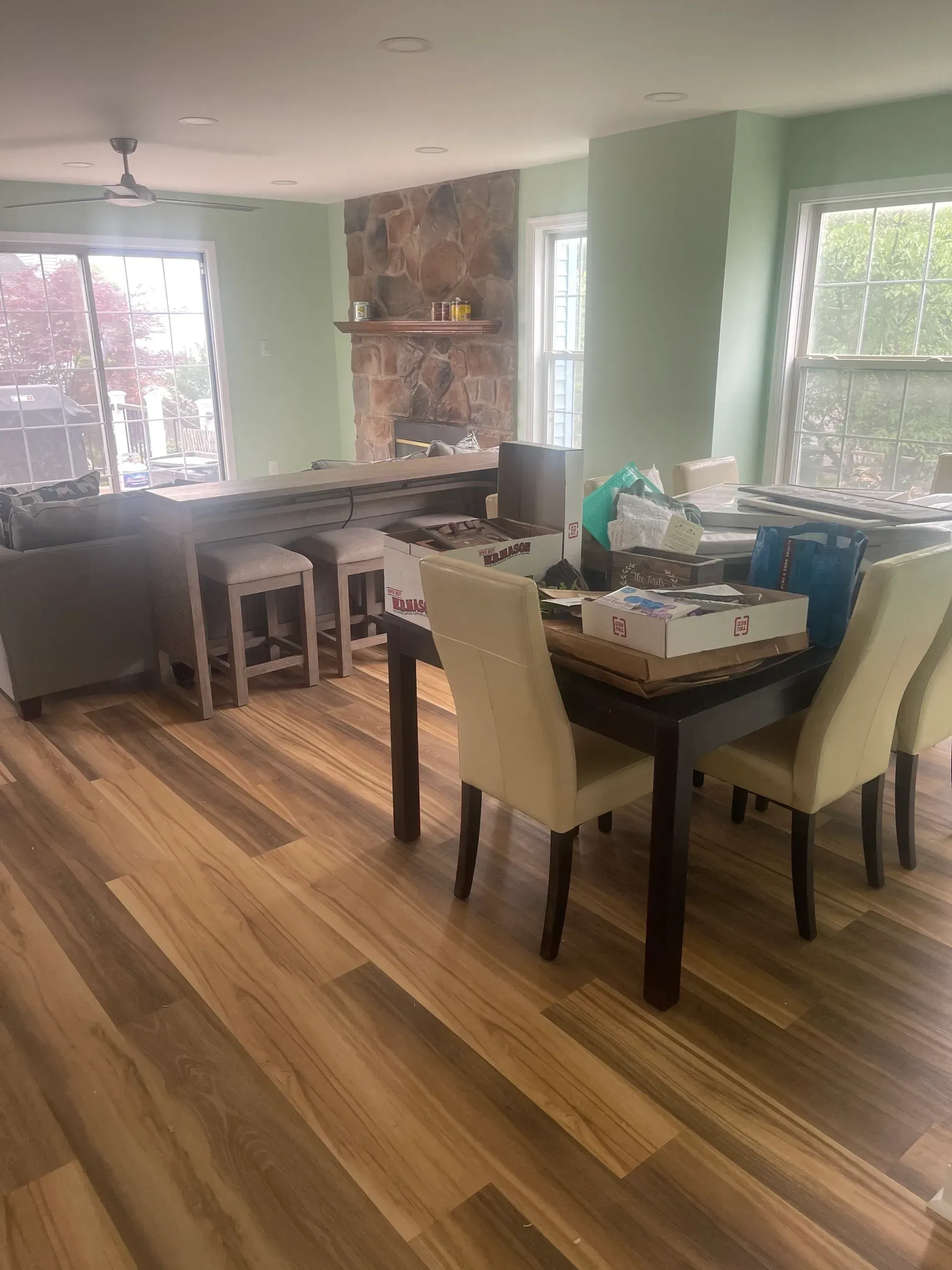 Dining area with table, chairs, bar stools, and fireplace, light green walls, wood floors.