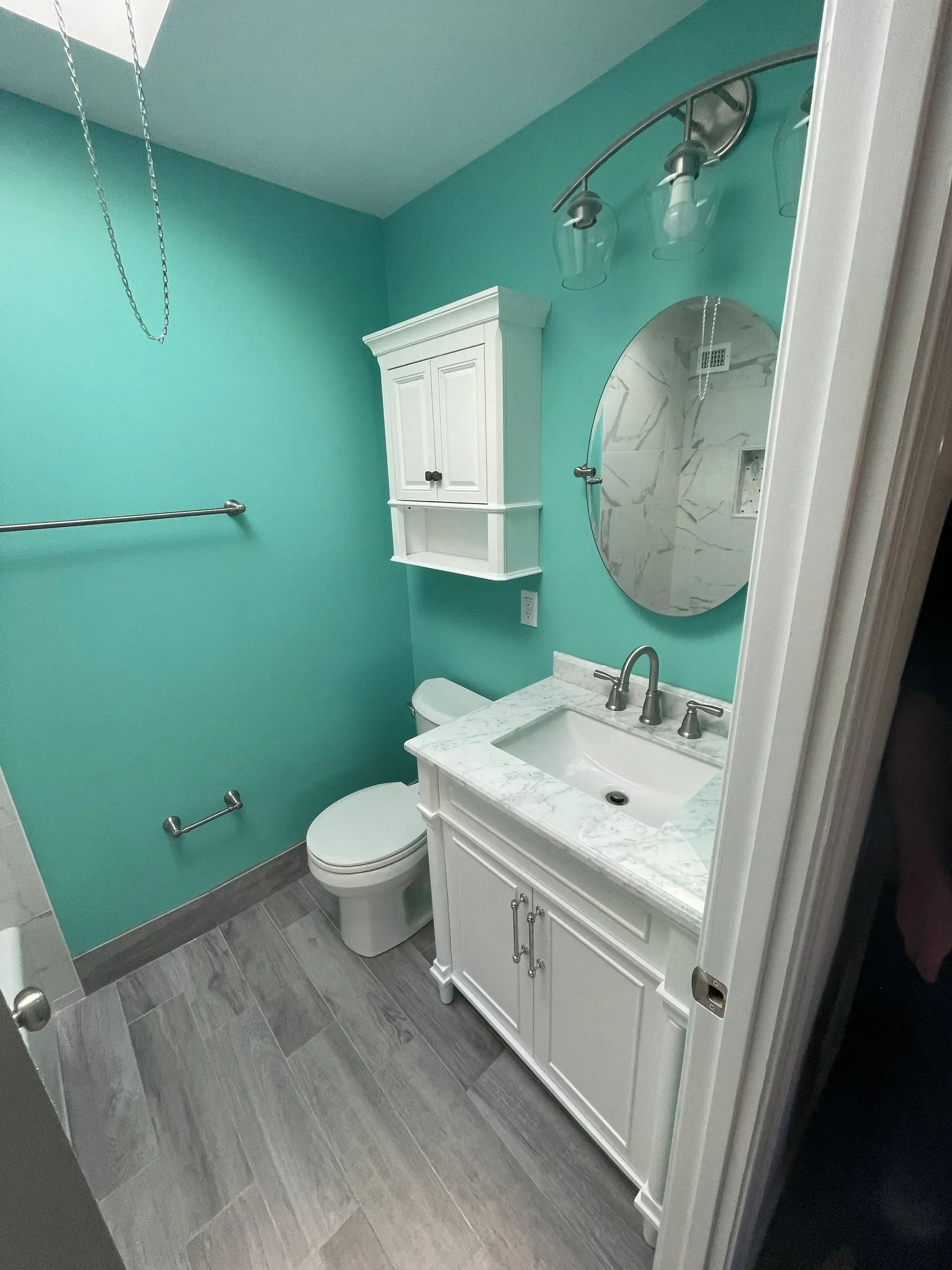 Bathroom with teal walls, white vanity, round mirror, and gray floor.